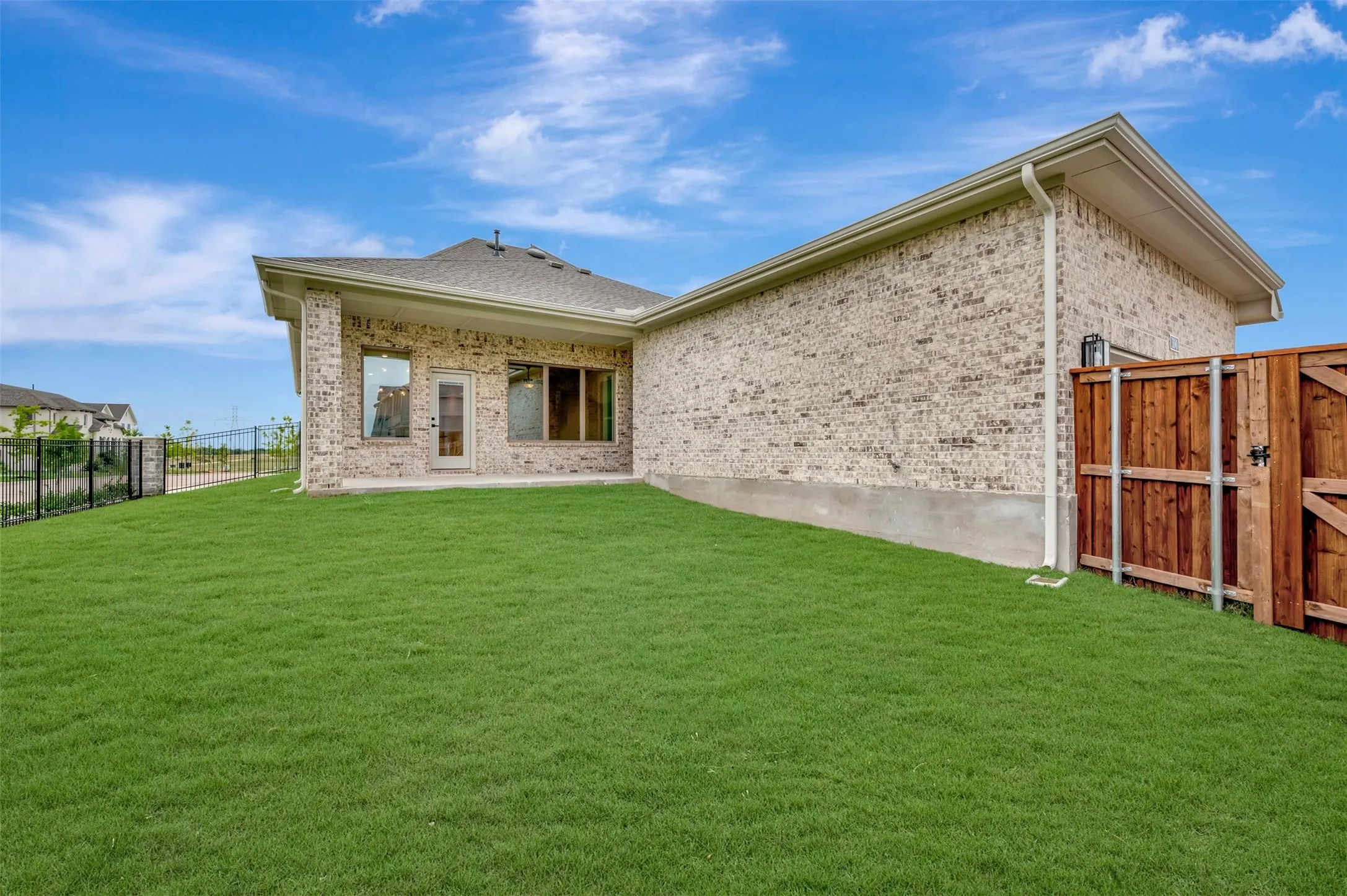Expansive rear lawn featuring a privacy fence, brick exterior, covered patio, rear entry door, and large windows
