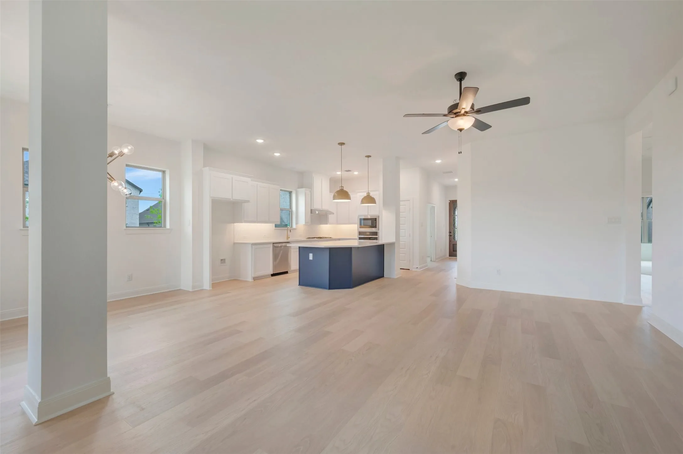Open-concept living area with light wood-finish flooring, white walls, and a modern ceiling fan