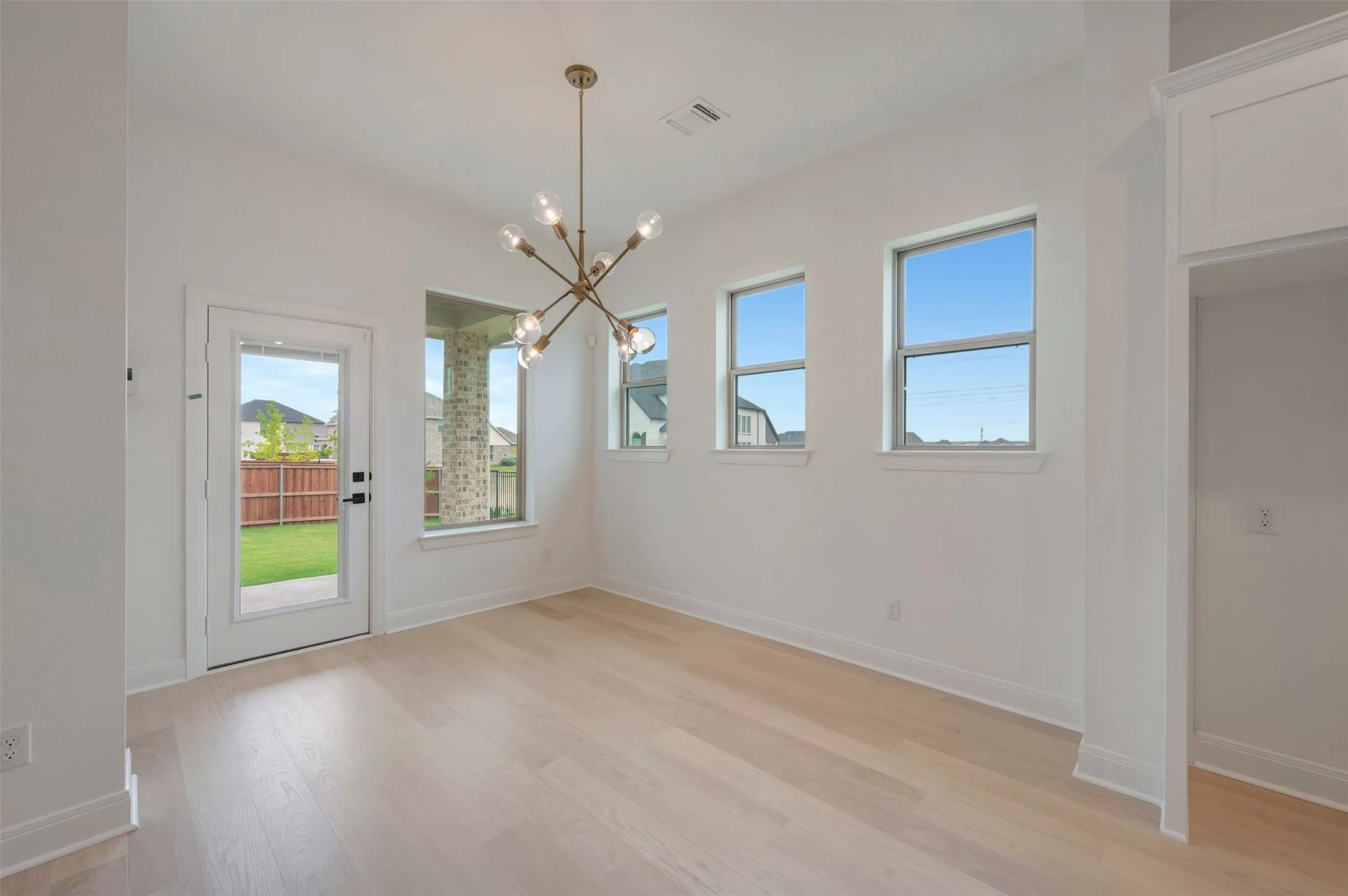 Bright interior space featuring light wood-finish flooring, multiple windows, a rear glass-paneled door, and a modern brass chandelier
