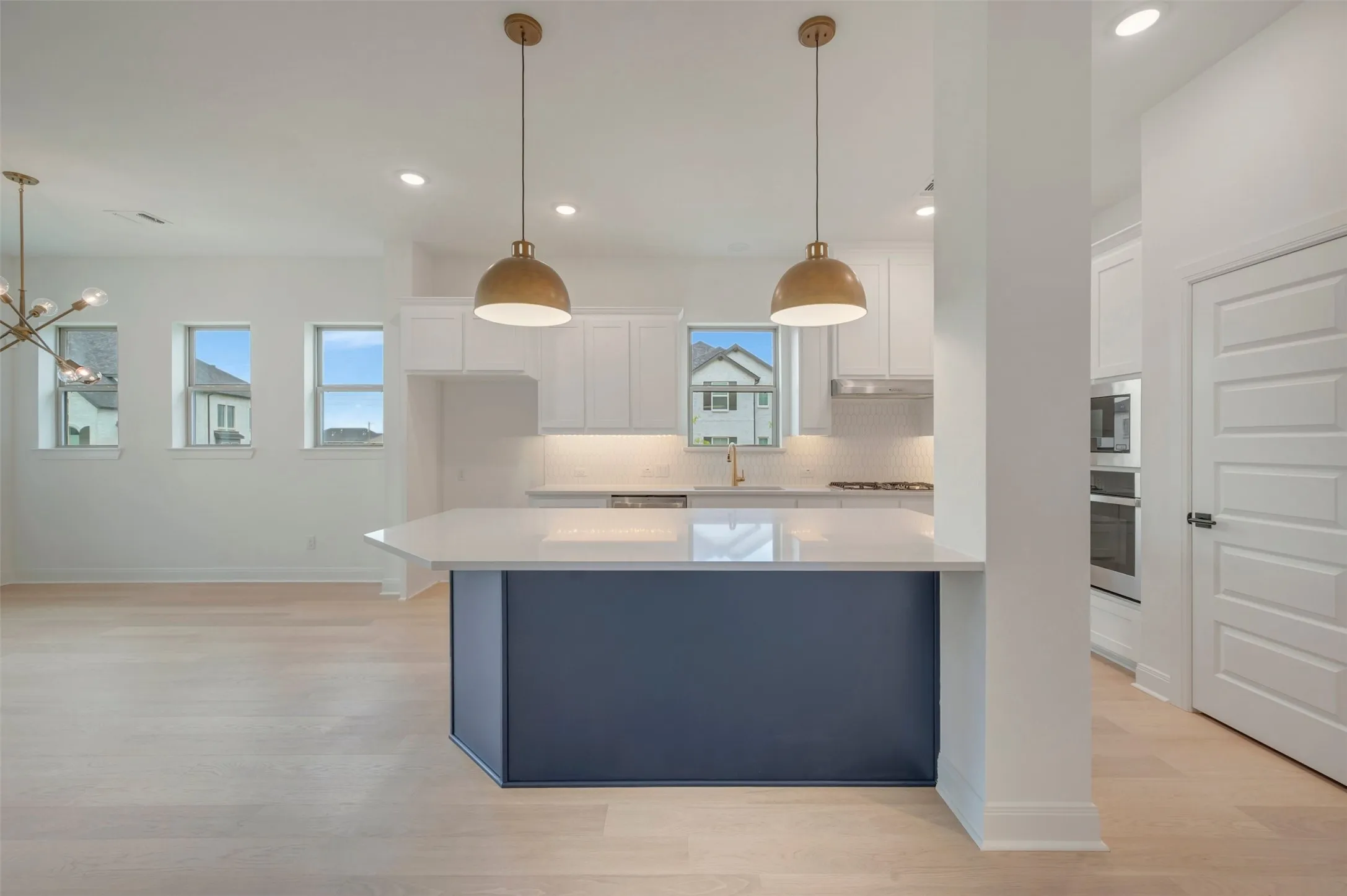 Contemporary kitchen island with a quartz countertop, pendant lighting, built-in double ovens, and light wood-finish flooring