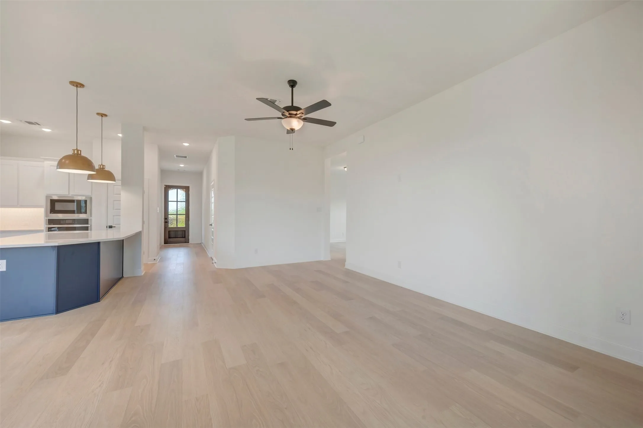 Open-concept living space featuring wood-finish flooring, a contemporary ceiling fan, and a kitchen island with pendant lighting