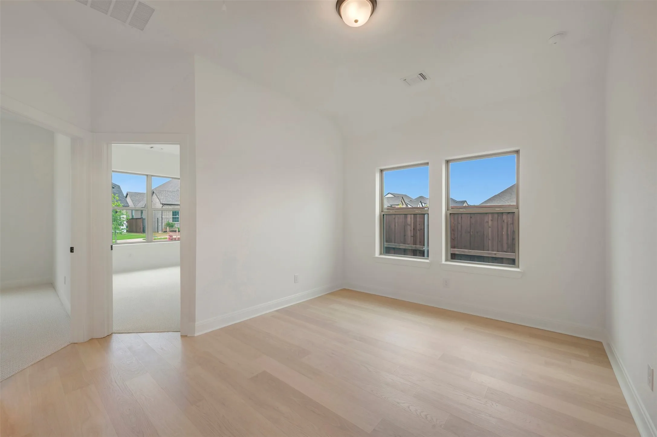 Spacious room with light wood-finish flooring, white walls, and a semi-flush mount ceiling light