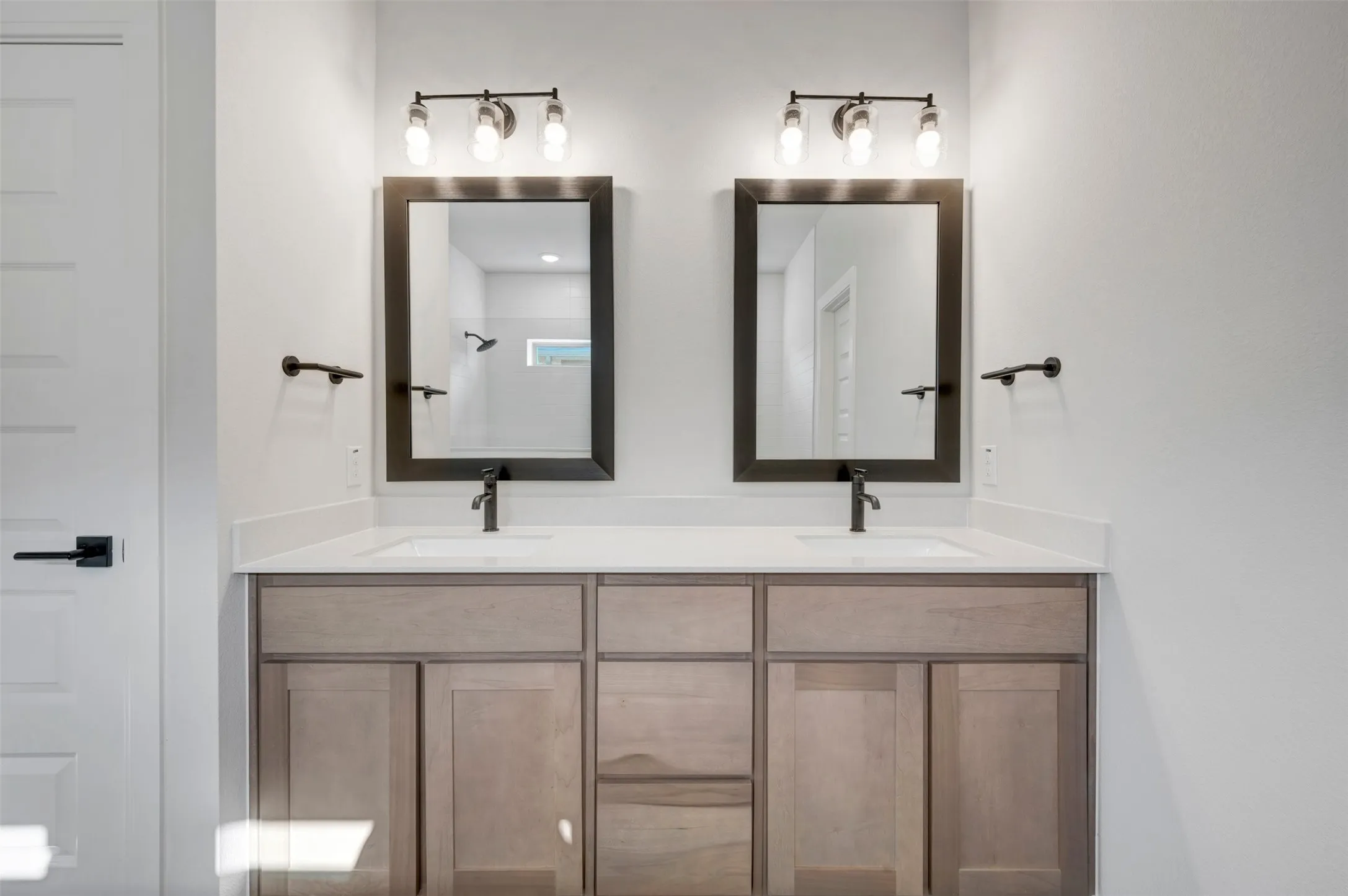 Dual vanity featuring light wood-finish cabinetry, white countertops, and matte black fixtures