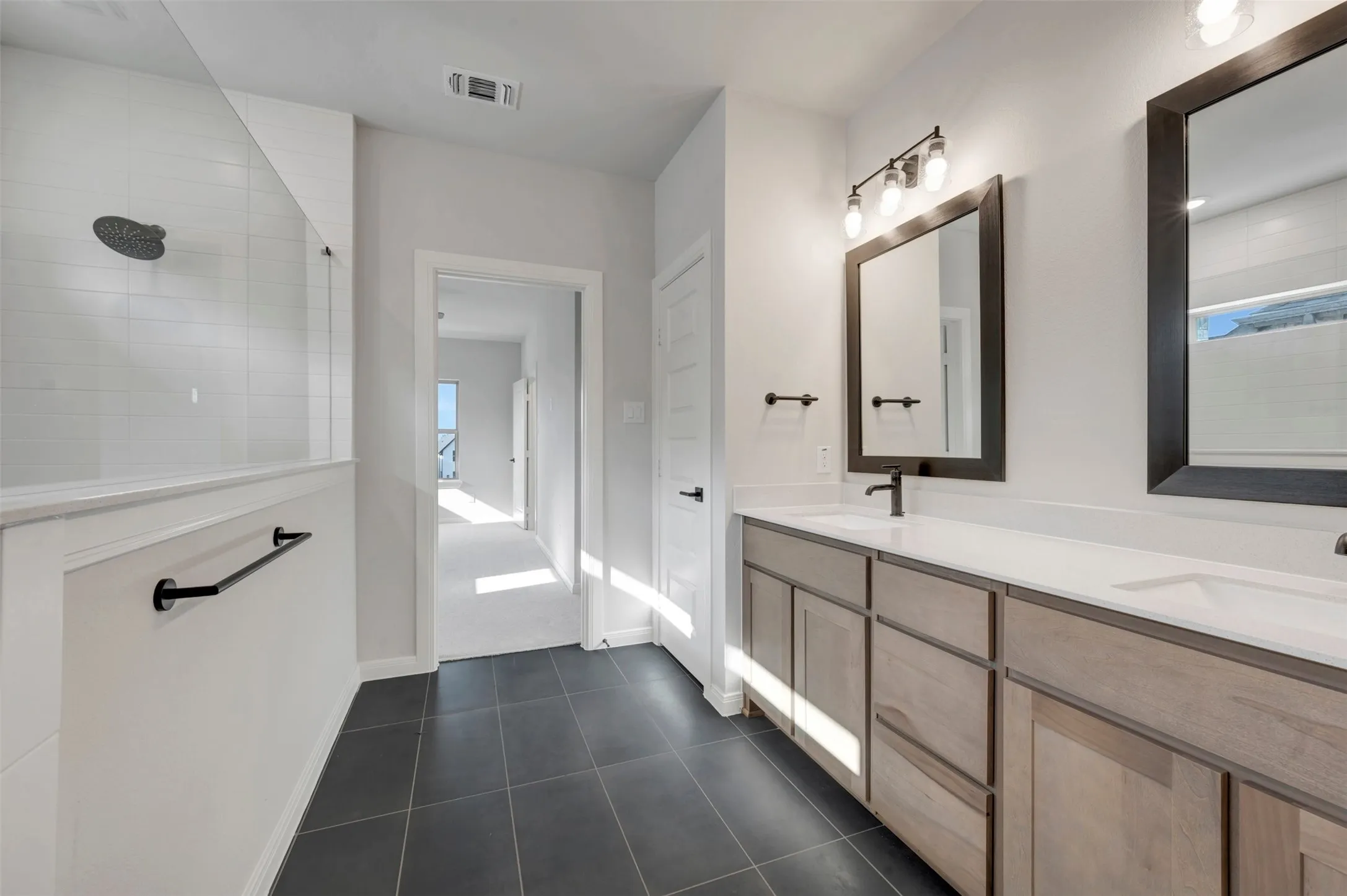 Bathroom featuring a dual vanity with light wood-finish cabinetry, white countertops, and black fixtures