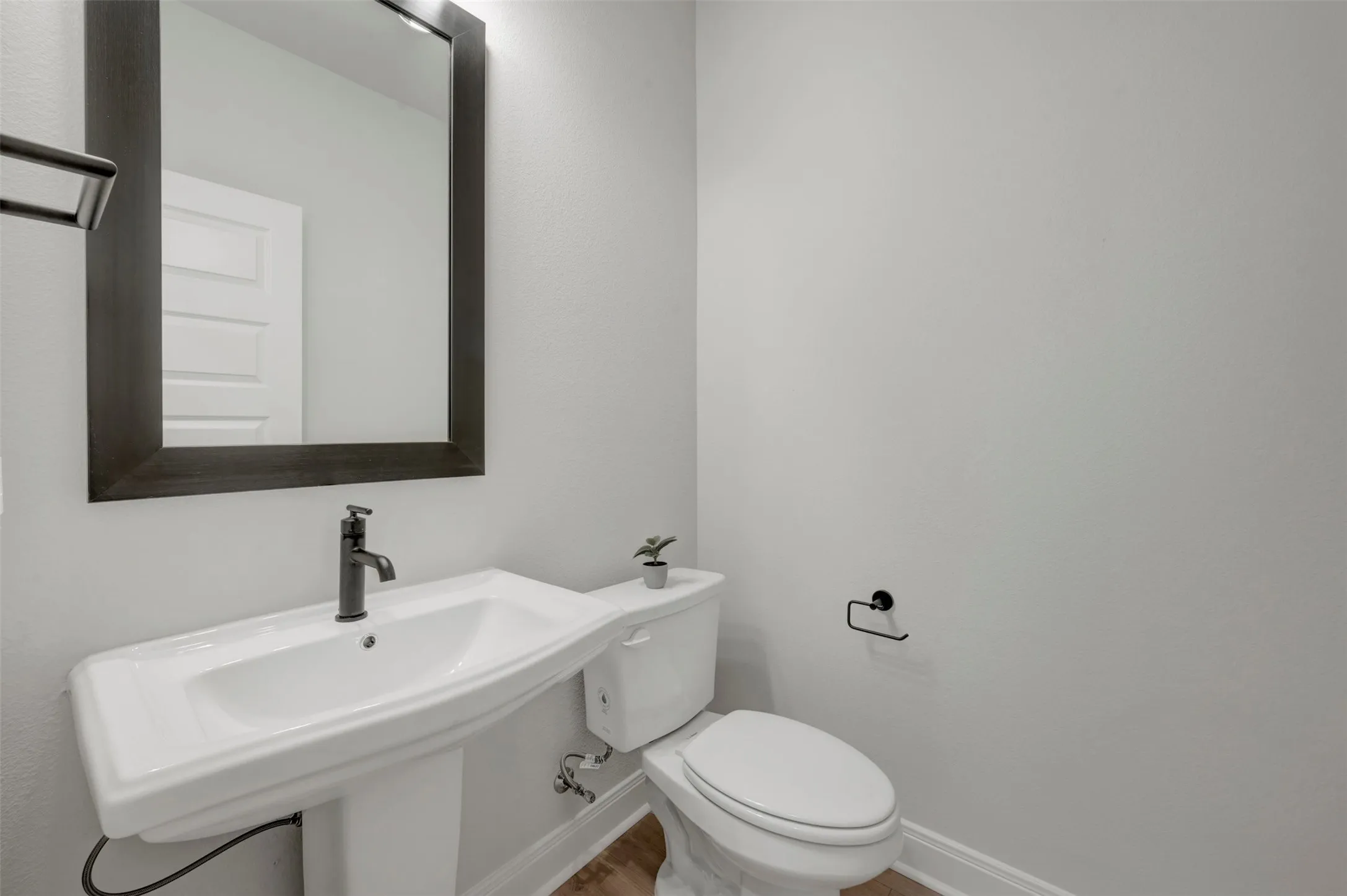 Modern bathroom featuring a pedestal sink with a matte black faucet, framed mirror, and wood-finish flooring