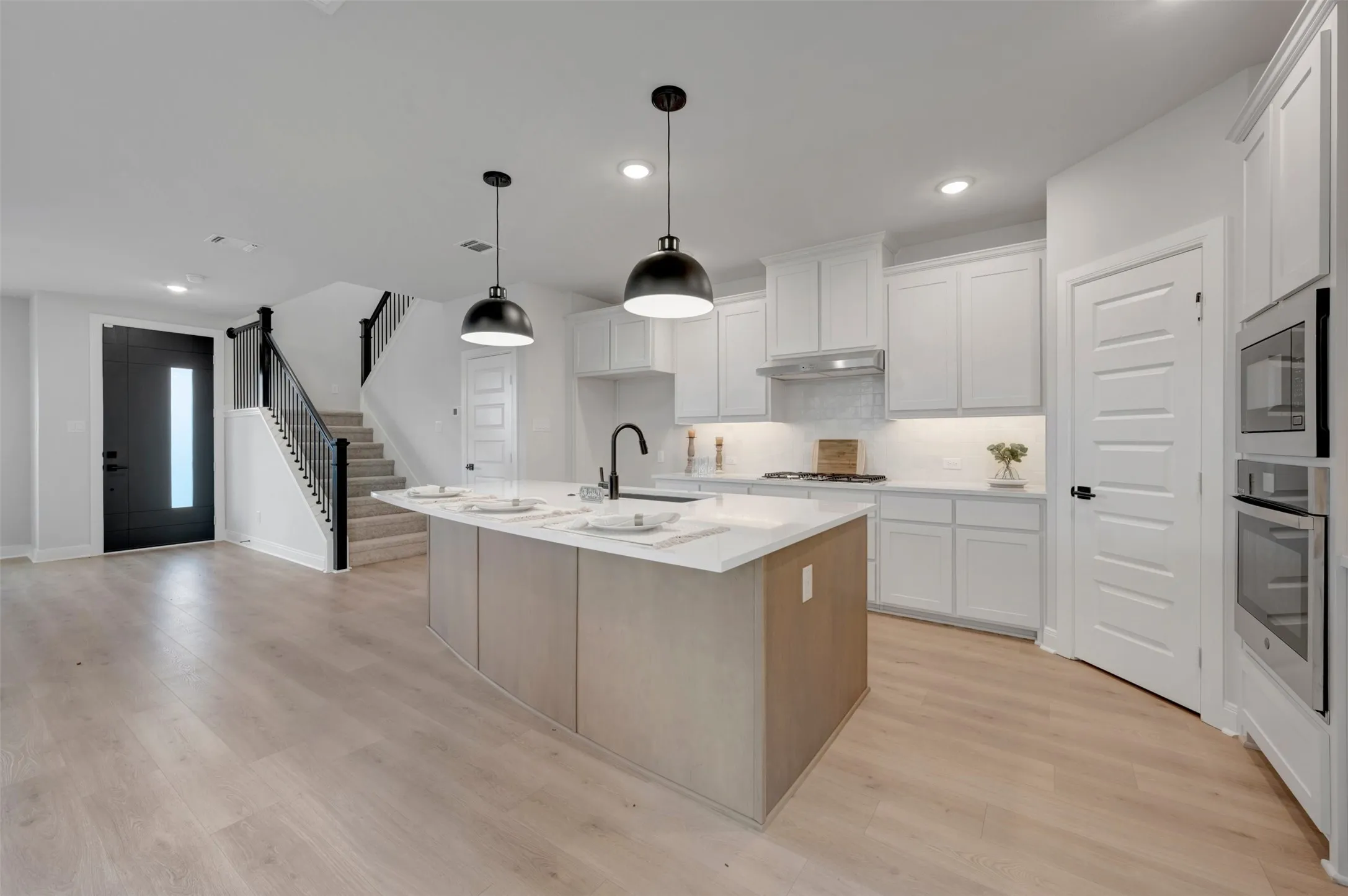 Modern kitchen featuring a central island with a sink, white cabinetry, integrated stainless steel appliances, and wood-finish flooring