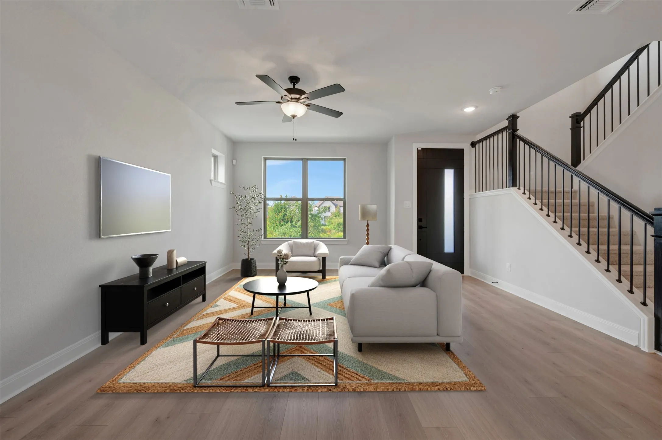 Open-concept living area featuring wood-finish flooring, a contemporary ceiling fan, and a large window providing ample natural light