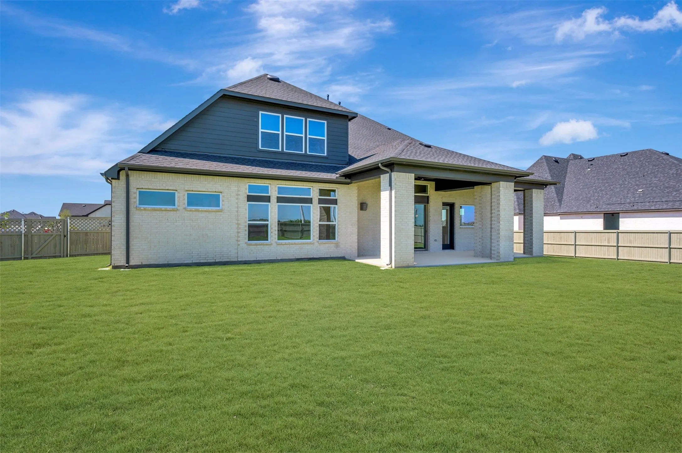 Expansive green lawn with a covered patio featuring brick columns and direct access to the interior