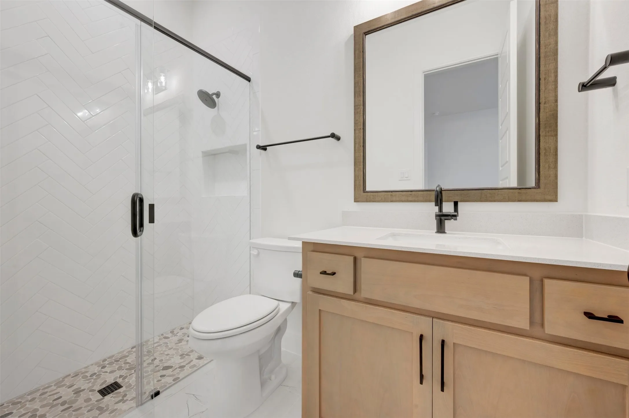 Contemporary bathroom featuring a light wood-finish vanity with a white countertop and undermount sink, a matte black faucet, and a frameless glass shower enclosure