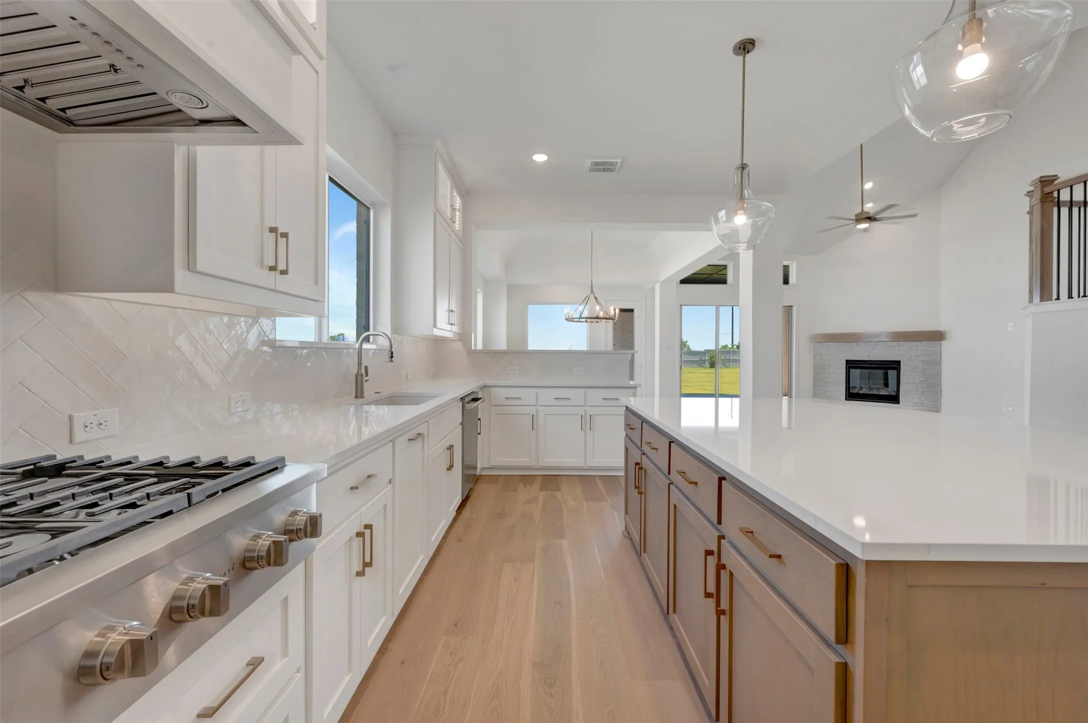 Gourmet kitchen featuring a stainless steel gas range, white shaker cabinetry, herringbone tile backsplash, an expansive center island with countertop seating, and light wood-finish flooring
