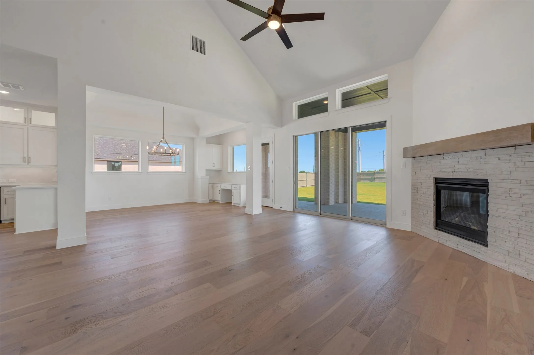 Spacious living area featuring wood-finish flooring, a stone-surround fireplace with a wood mantle, and a vaulted ceiling with a ceiling fan