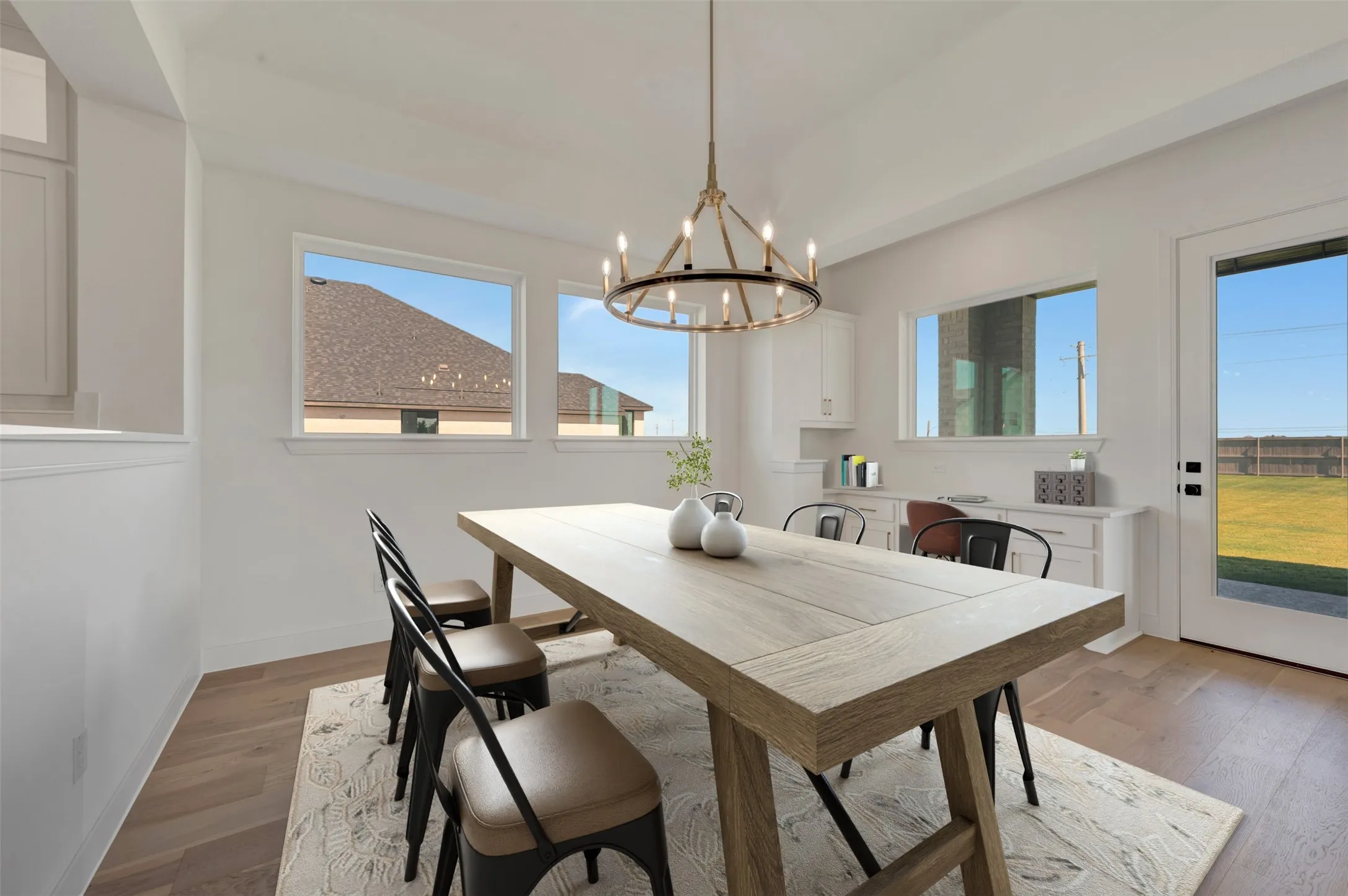 Spacious interior room featuring wood-finish flooring, multiple windows, a ceiling-mounted chandelier, and built-in cabinetry with a countertop