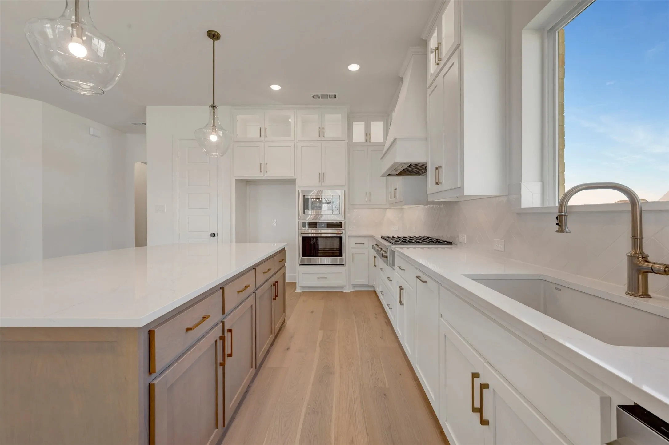 Spacious kitchen featuring an expansive center island with light wood-finish cabinetry, white countertops, a gas range, and integrated double ovens