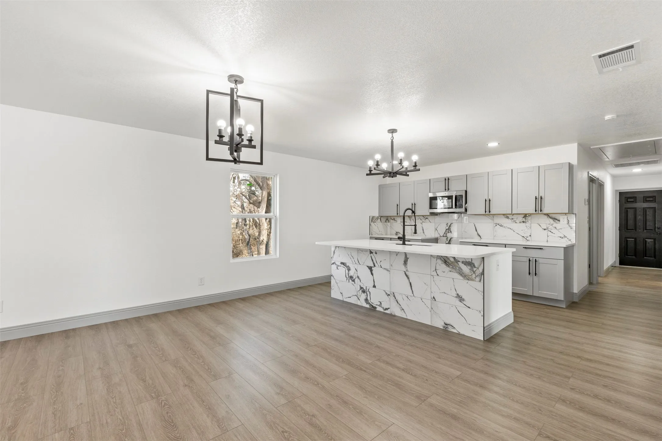Kitchen with gray cabinetry, a center island with sink, stainless steel microwave, and a chandelier