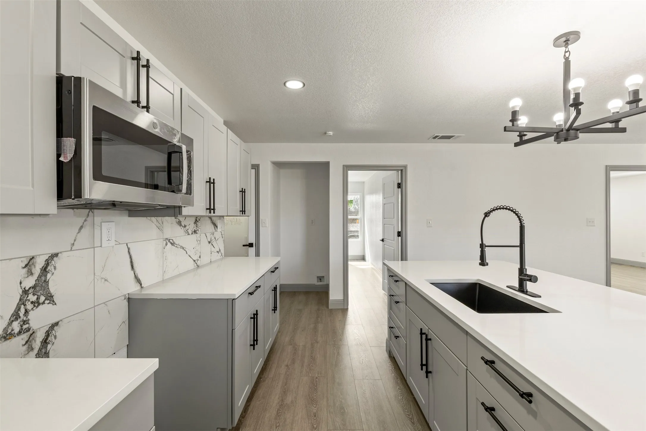Kitchen with stainless steel microwave, gray cabinetry, light stone countertops, light wood-style floors, and a textured ceiling