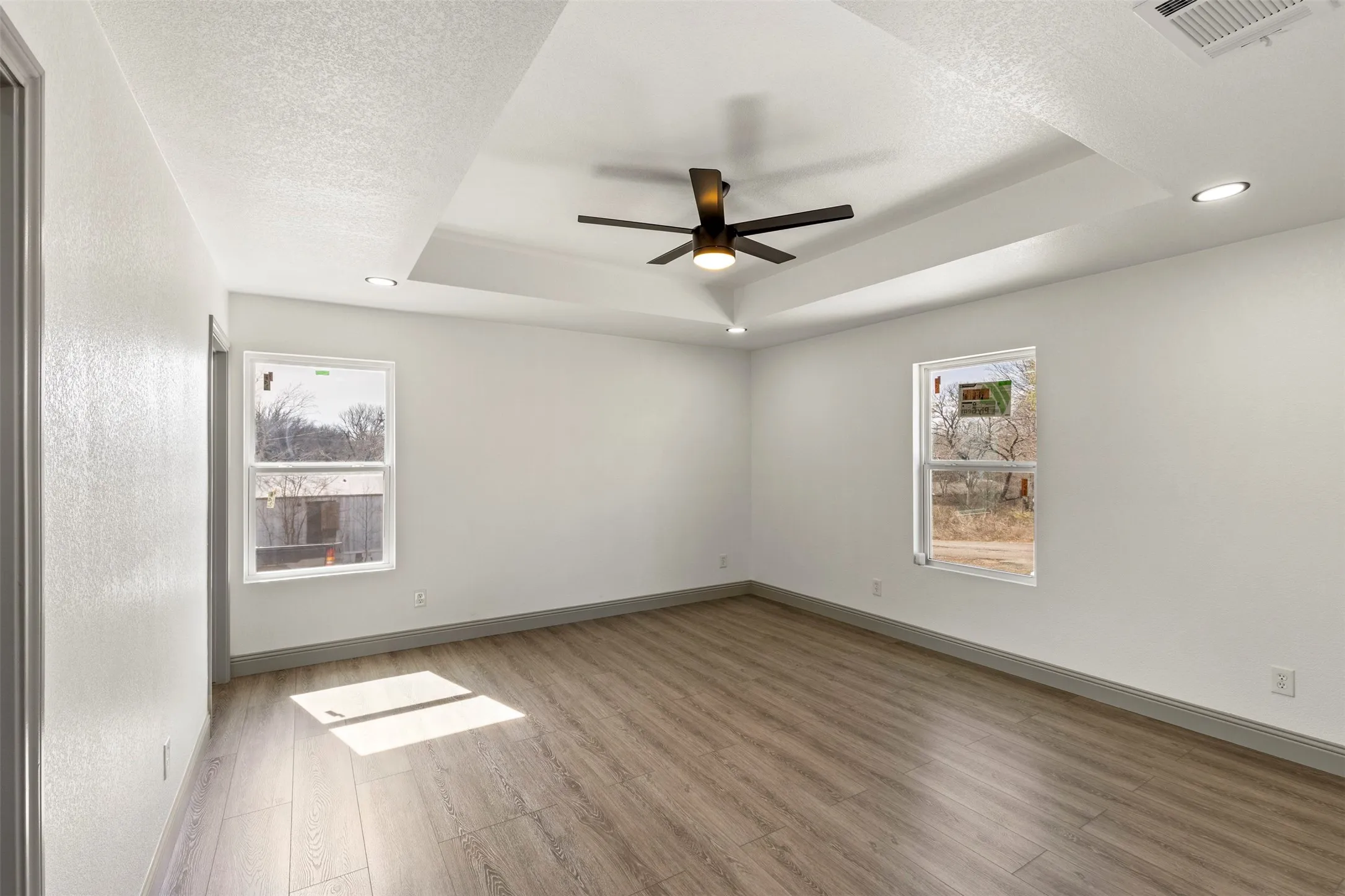 Empty room with a ceiling fan, light wood finished floors, a textured ceiling, recessed lighting, and a raised ceiling