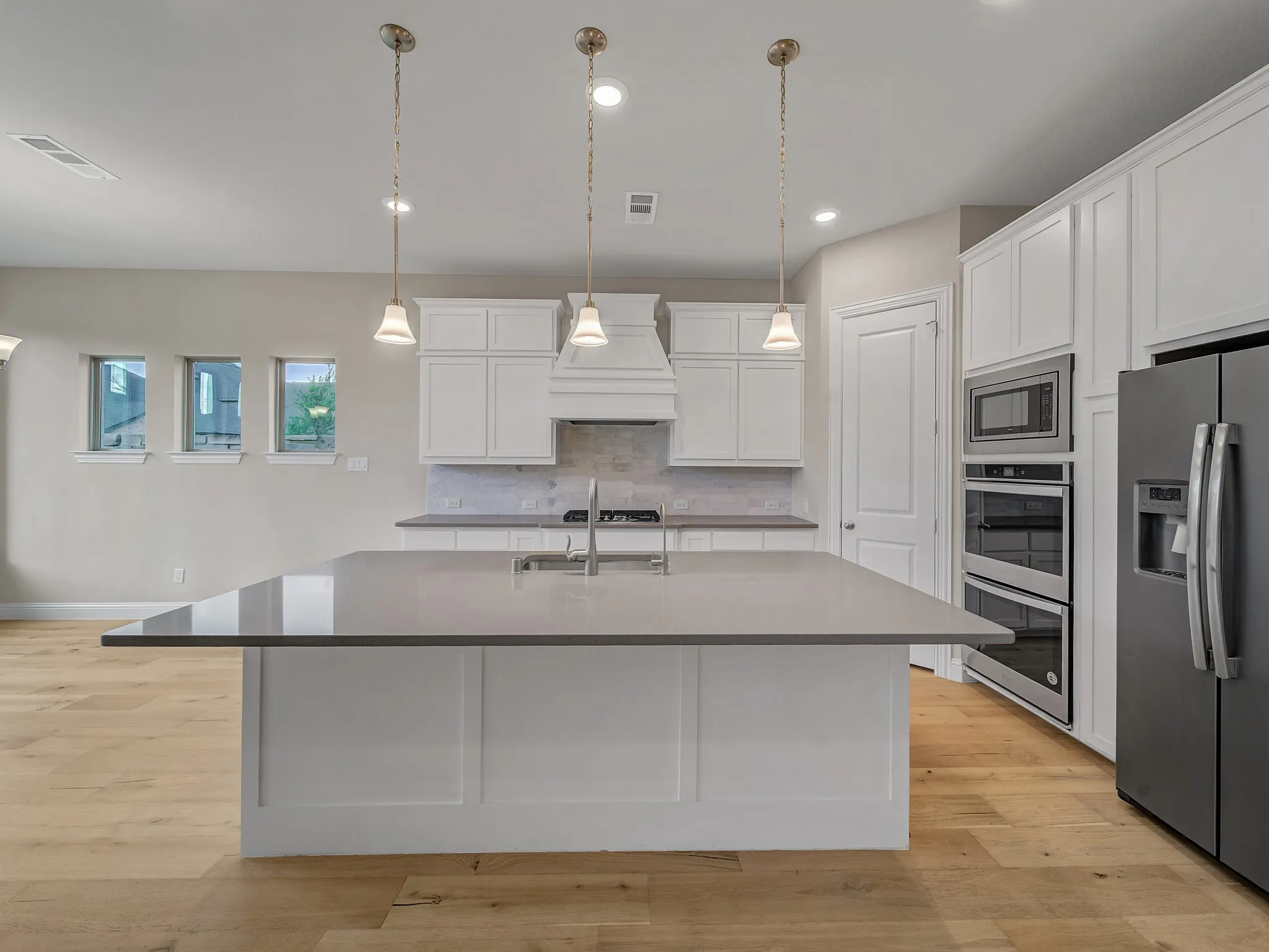 Kitchen with stainless steel appliances, white cabinets, light wood-type flooring, a kitchen island with sink, and recessed lighting