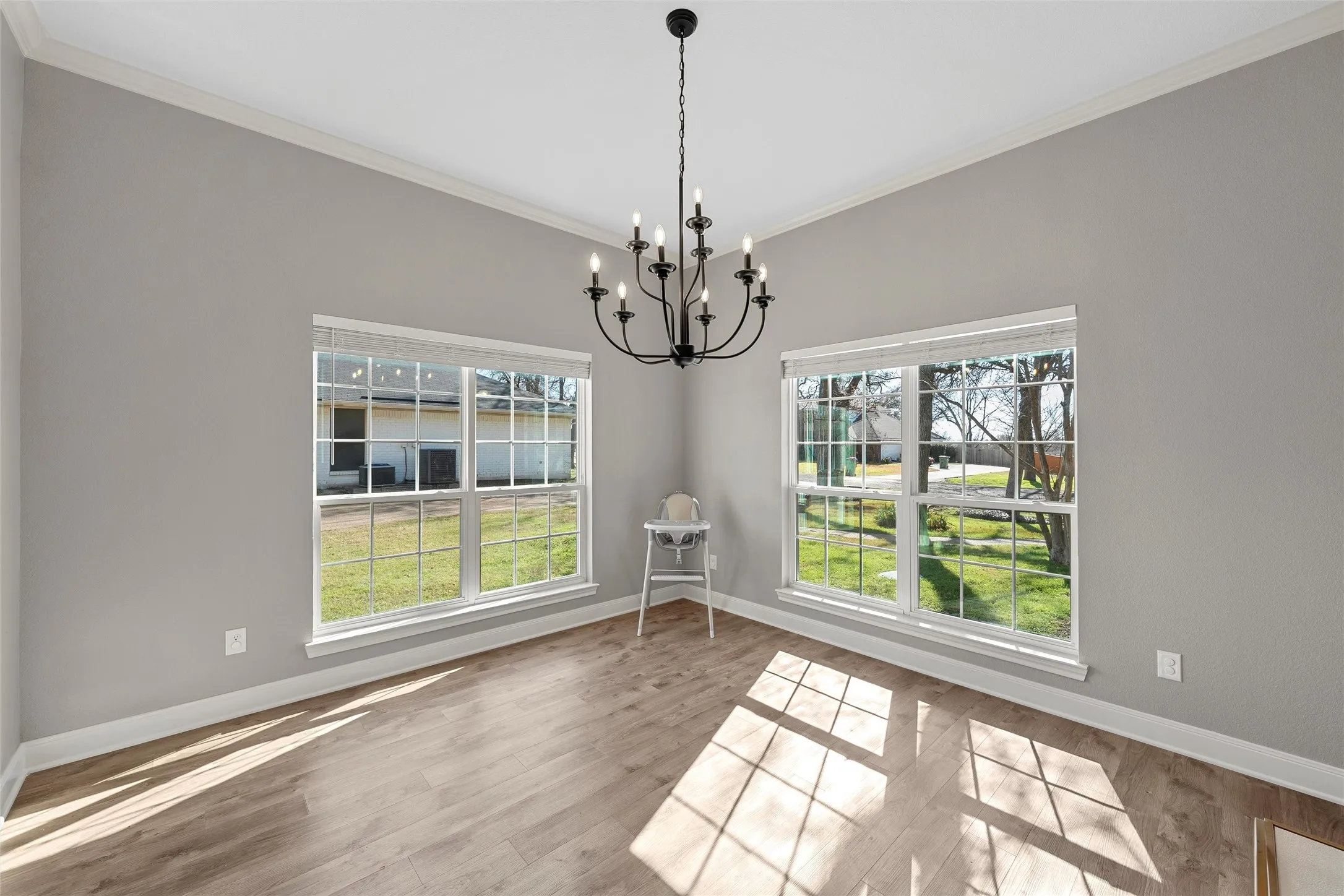 Sun-drenched formal dining room with oversized grid windows flooding the space with natural light, crown molding, wood-look floors, and statement black chandelier — 117 Lost Oaks Drive, Waco TX 76705.