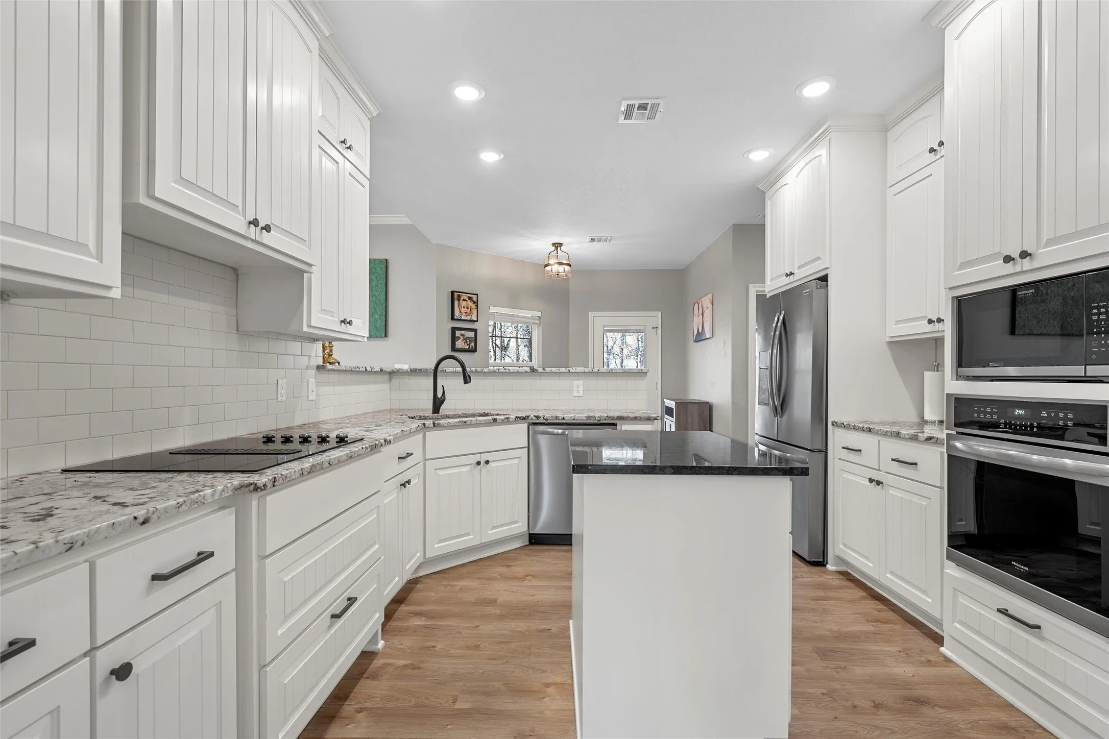 Updated kitchen with custom white shaker cabinetry, granite countertops, subway tile backsplash, center island, breakfast bar, and full stainless appliance package including cooktop, double wall oven, and French door refrigerator — 117 Lost Oaks Drive, Waco TX 76705.