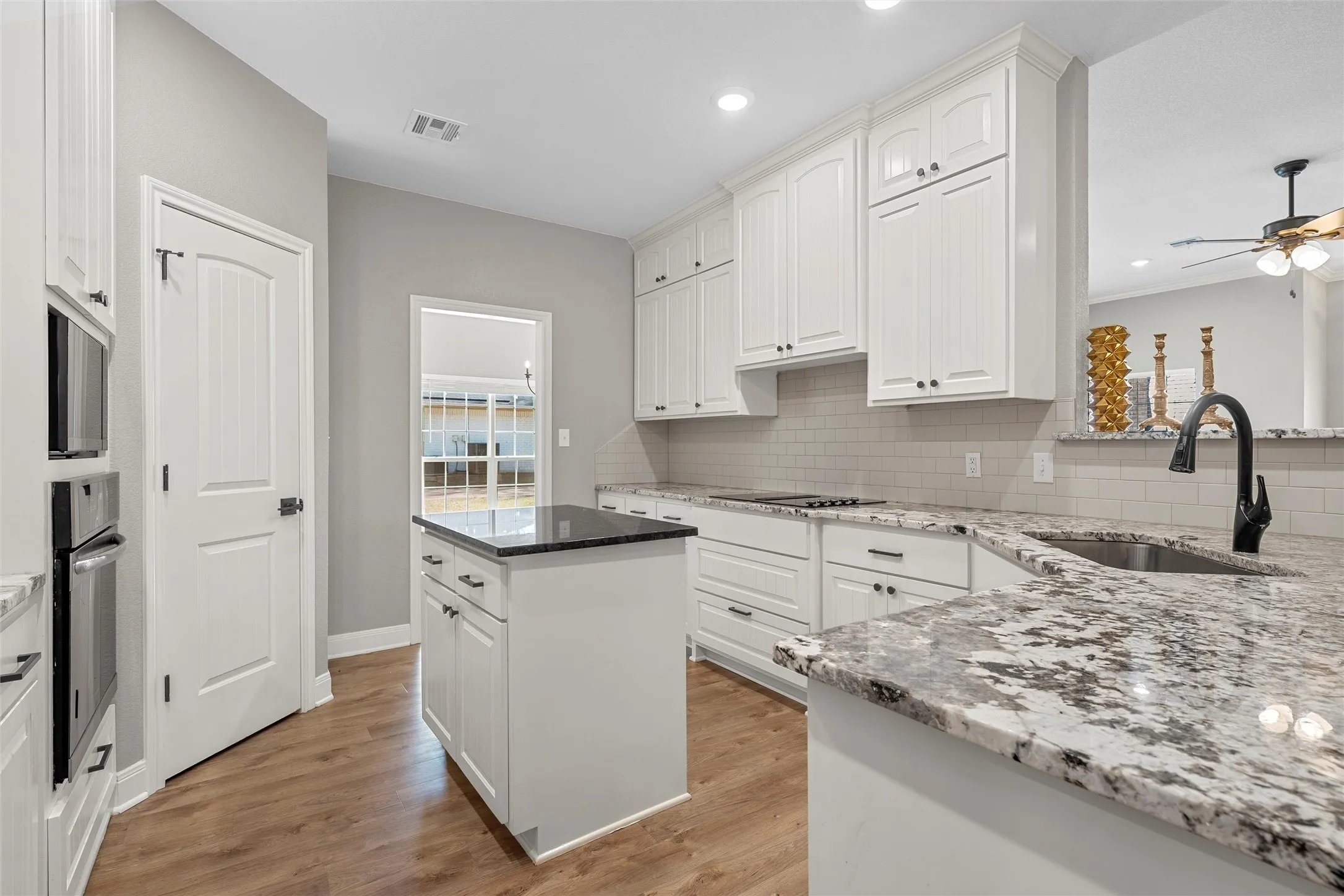 Updated kitchen with custom white shaker cabinetry, granite countertops, subway tile backsplash, center island, breakfast bar, and full stainless appliance package including cooktop, double wall oven, and French door refrigerator — 117 Lost Oaks Drive, Waco TX 76705.