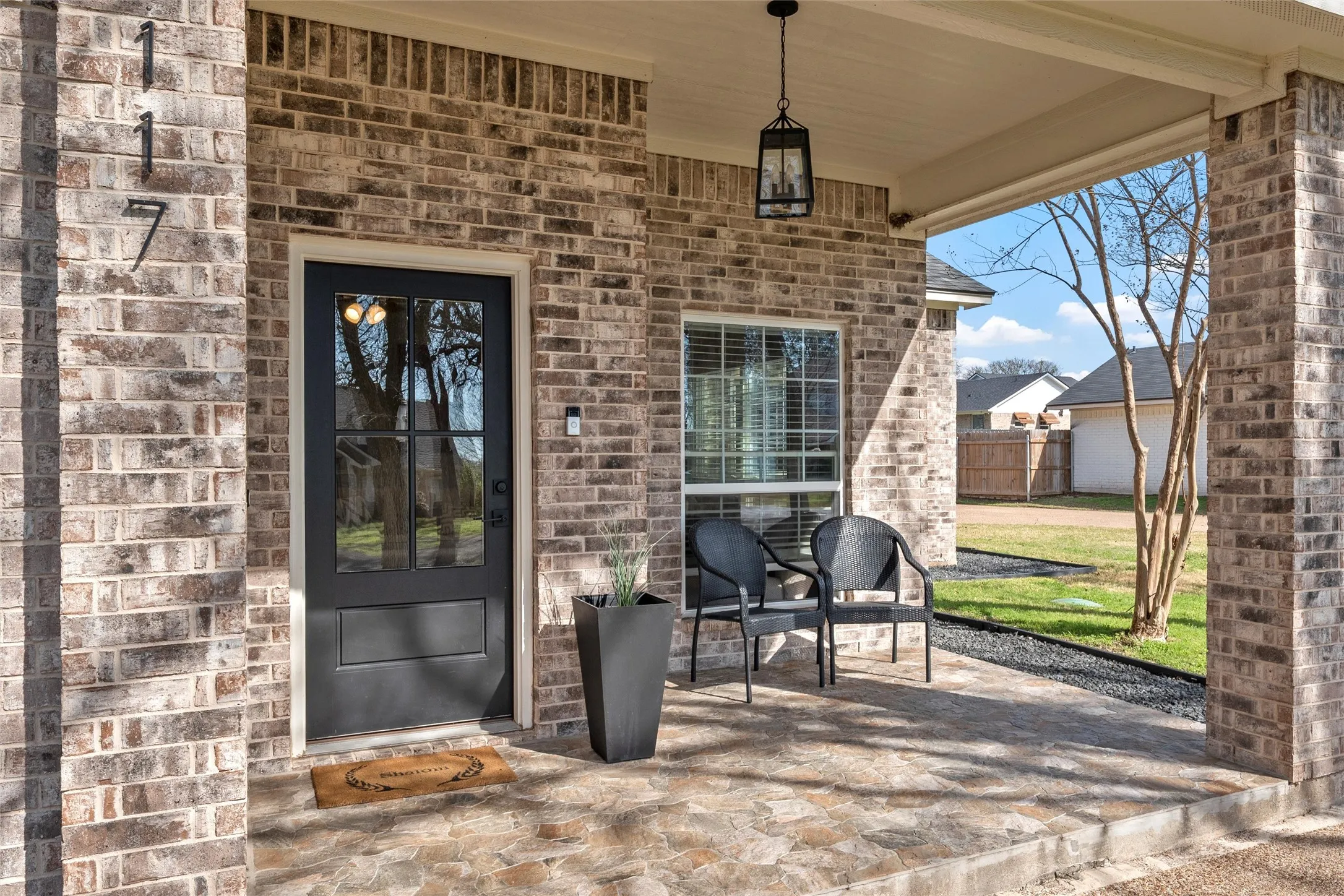 Brick exterior home at 117 Lost Oaks Drive, Waco TX 76705 with uplighting, mature oak canopy, modern concrete stepping stone path, and covered patio entry — exceptional curb appeal on a private lot surrounded by established trees.