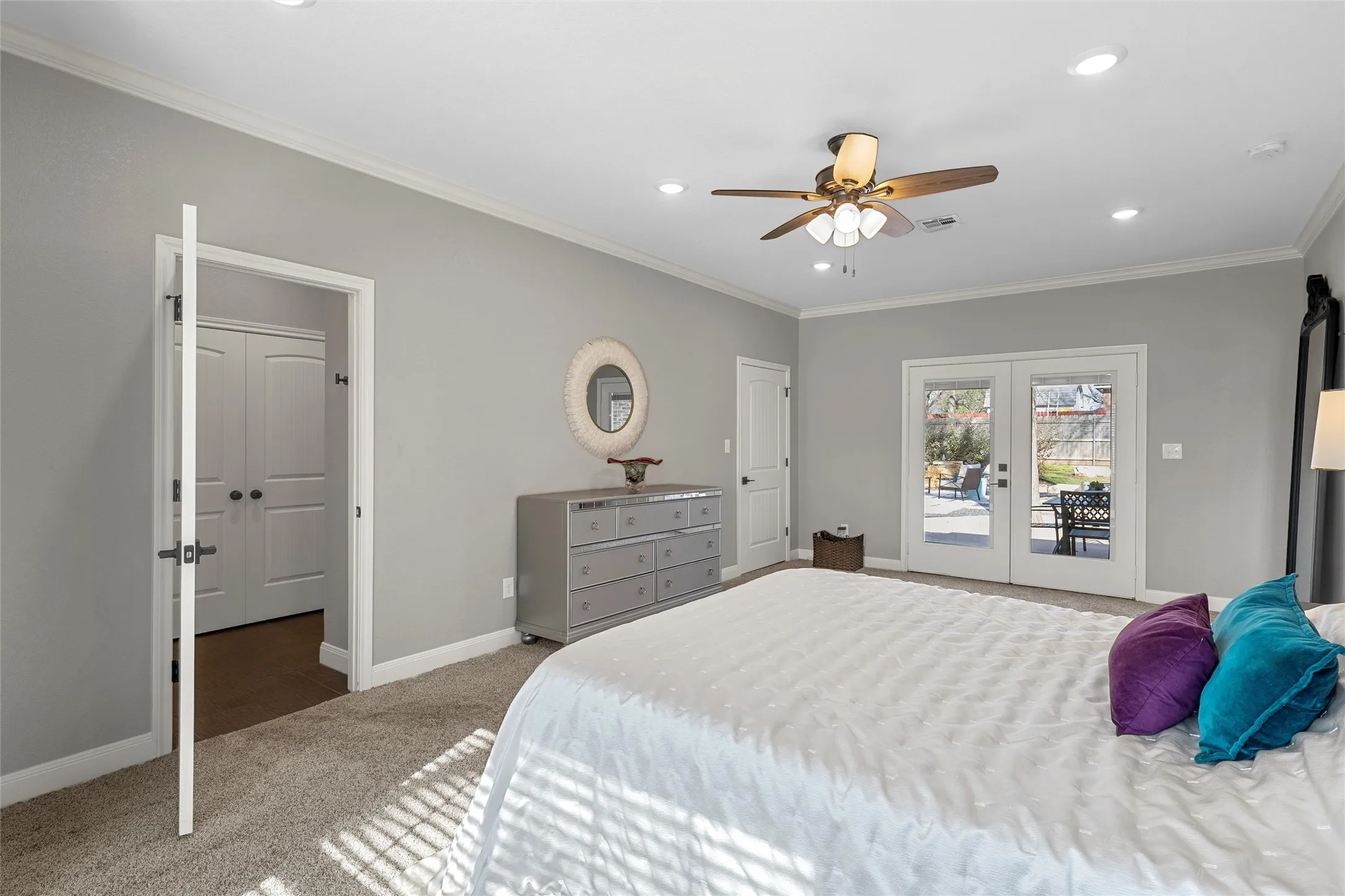 Expansive primary bedroom with plush carpet, crown molding, recessed lighting, ceiling fan, and French doors opening directly to the covered back patio — a private retreat at 117 Lost Oaks Drive, Waco TX 76705.