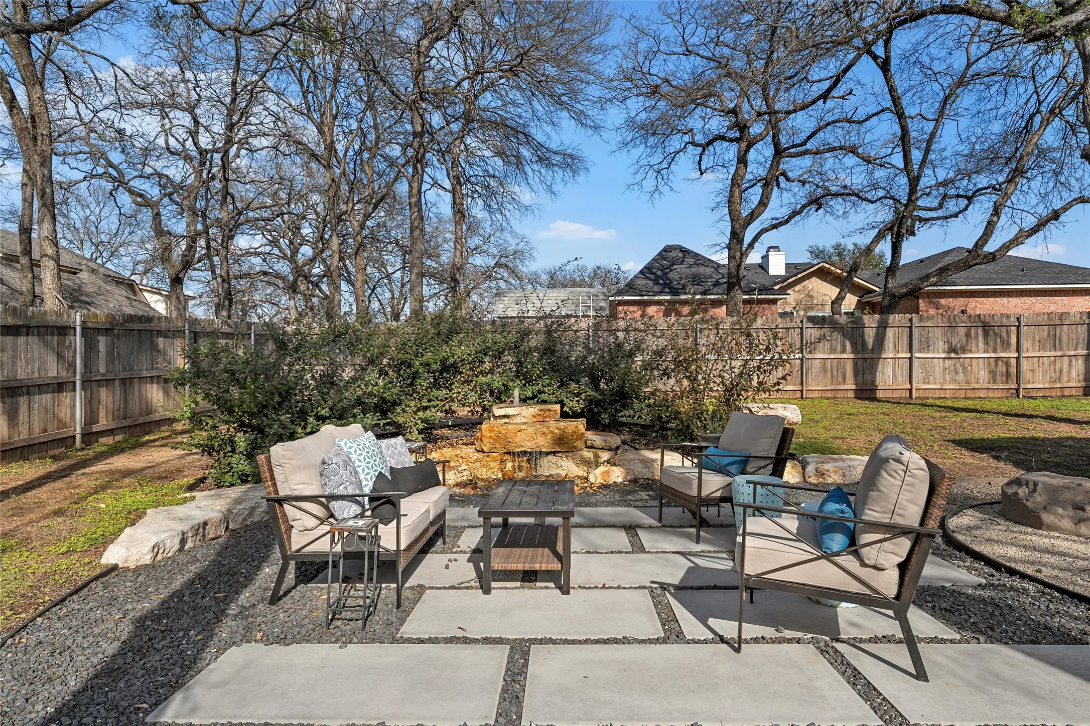 Private backyard retreat with expanded concrete patio, outdoor seating area, natural limestone water fountain feature, mature shade trees, and full wood privacy fence — outdoor living at its best at 117 Lost Oaks Drive, Waco TX 76705.