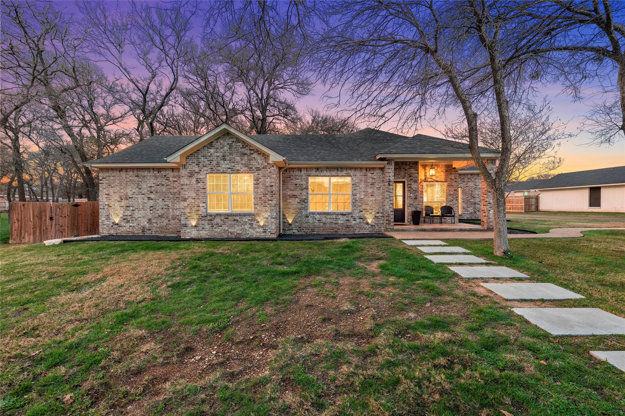 Brick exterior home at 117 Lost Oaks Drive, Waco TX 76705 with uplighting, mature oak canopy, modern concrete stepping stone path, and covered patio entry — exceptional curb appeal on a private lot surrounded by established trees.