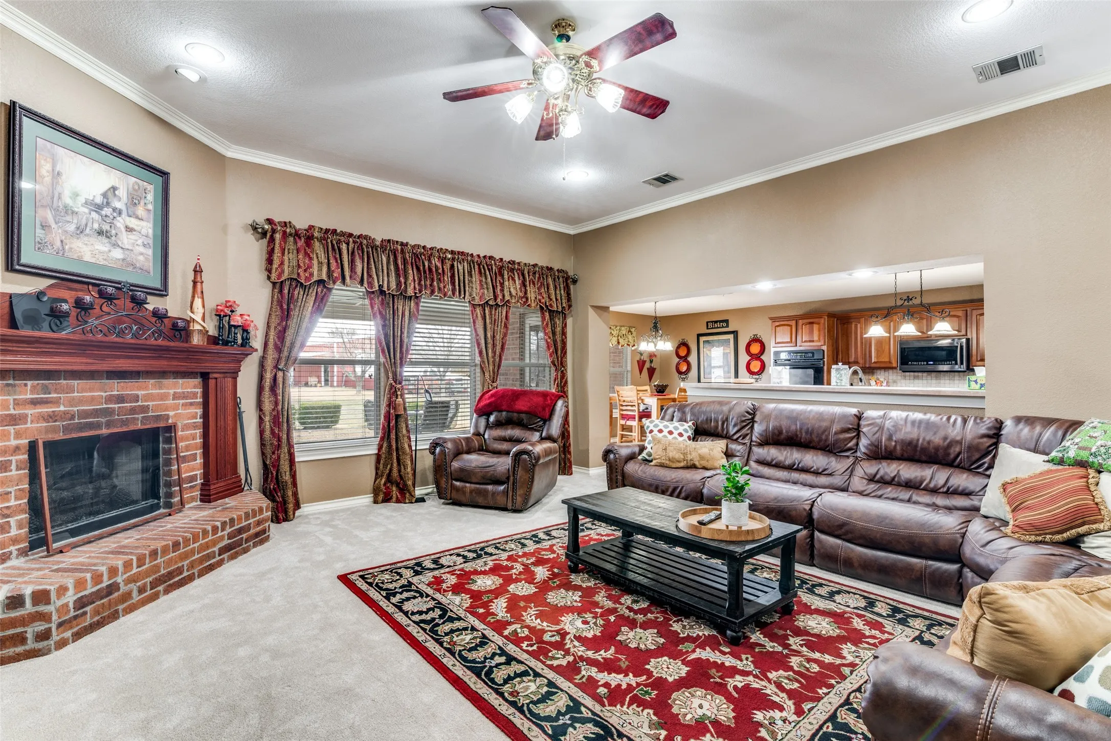 Living area featuring ornamental molding, ceiling fan, a fireplace, carpet, and suspended lighting