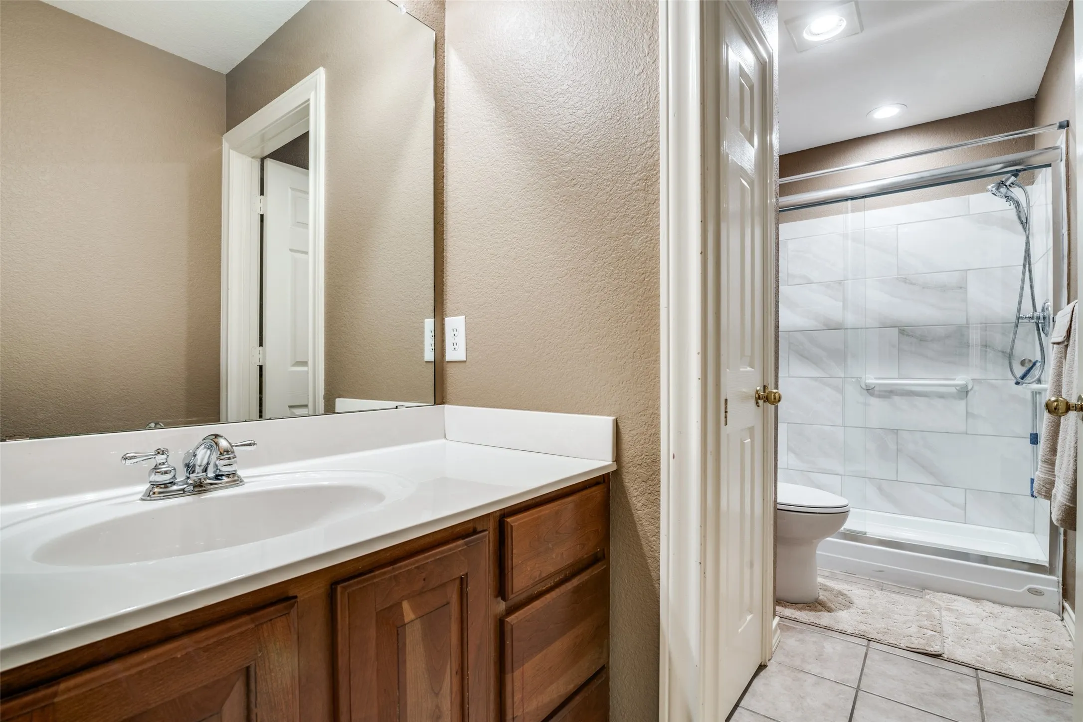 Bathroom featuring a textured wall, a shower stall, vanity, and light tile patterned floors
