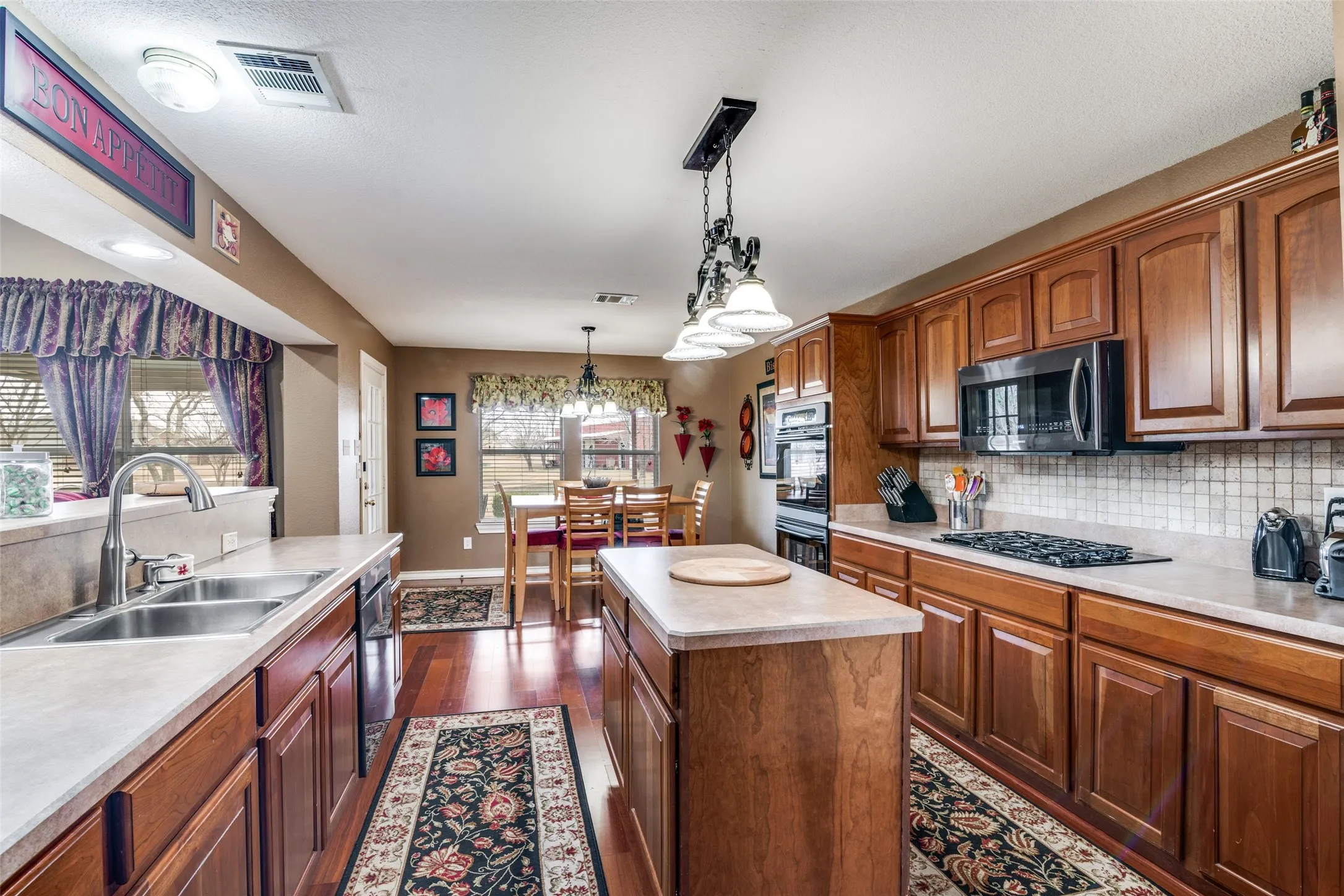 Kitchen with pendant lighting, light countertops, tasteful backsplash, a center island, and black appliances