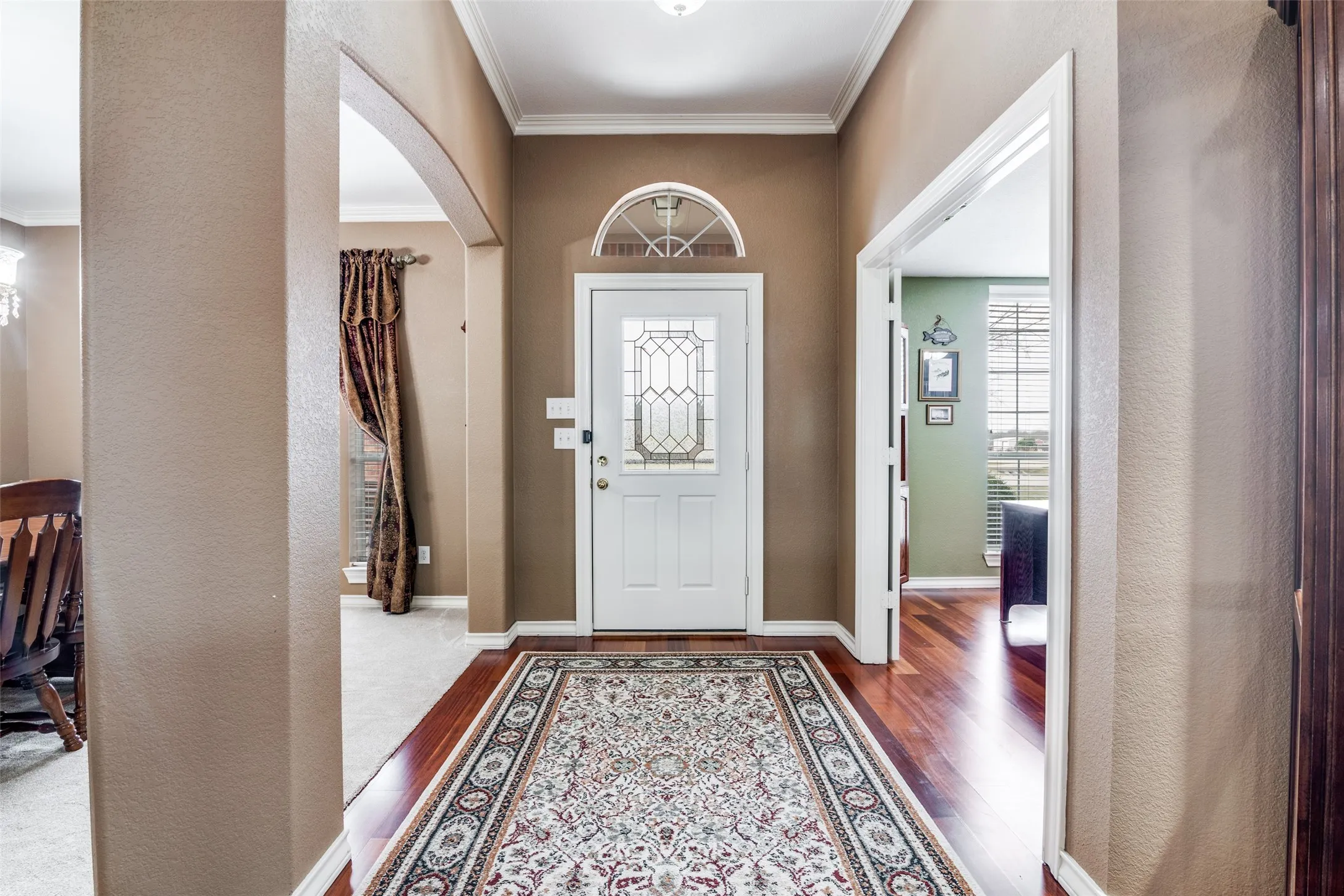 Entryway featuring arched walkways, crown molding, a textured wall, and wood finished floors