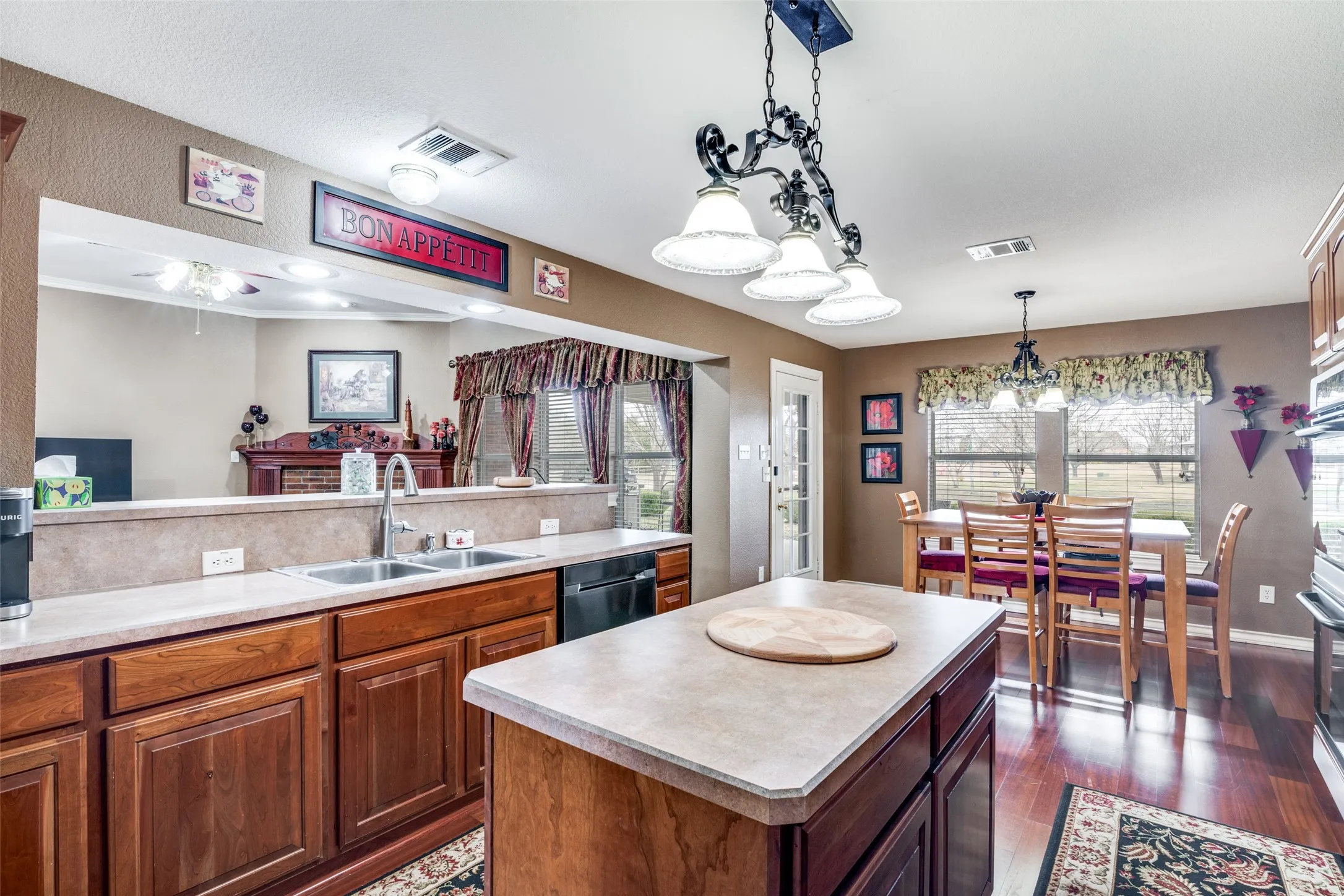 Kitchen featuring decorative light fixtures, a kitchen island, wood finish cabinetry, light countertops, and dishwasher