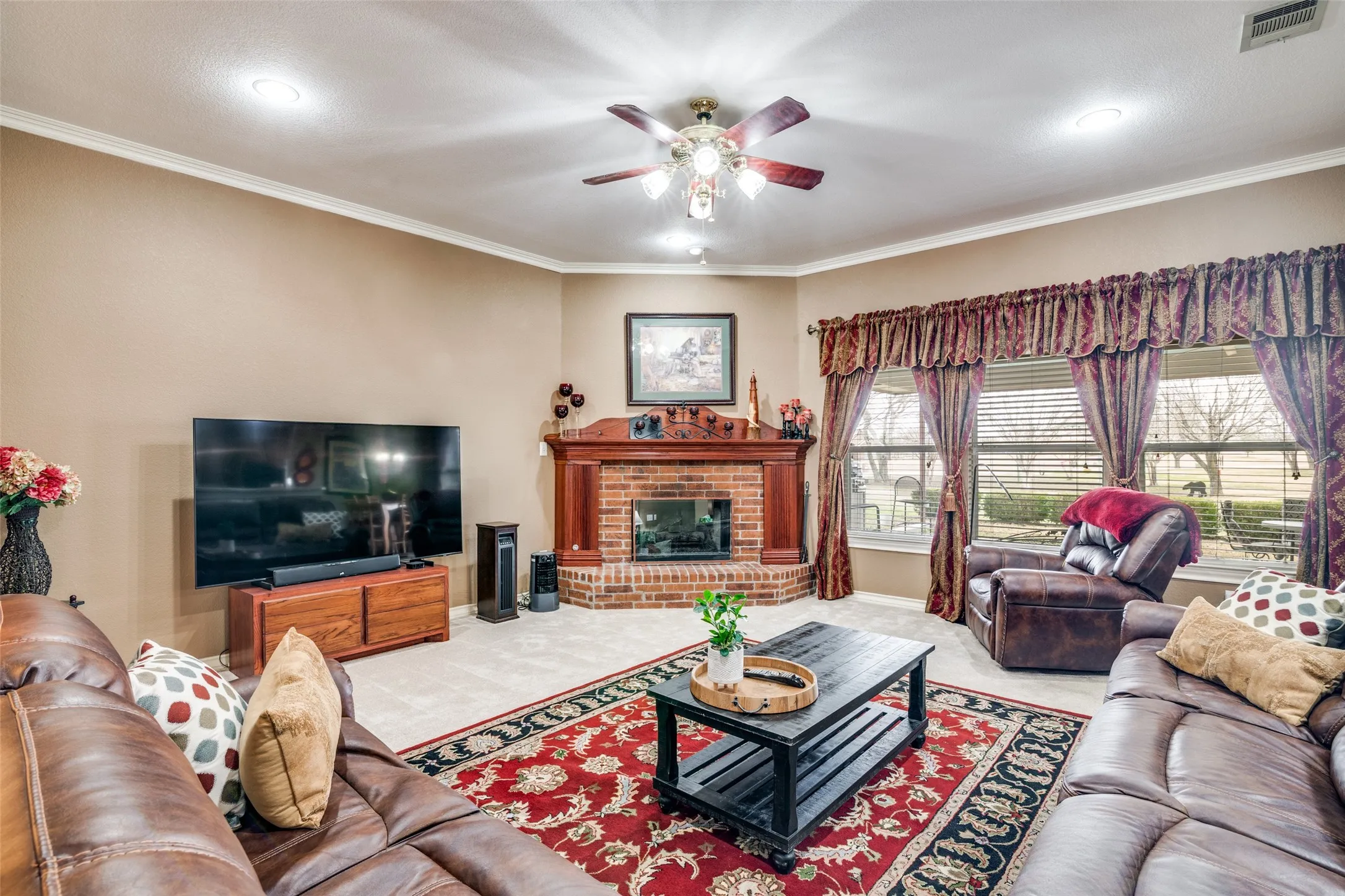 Living room featuring carpet floors, a fireplace, ceiling fan, and crown molding