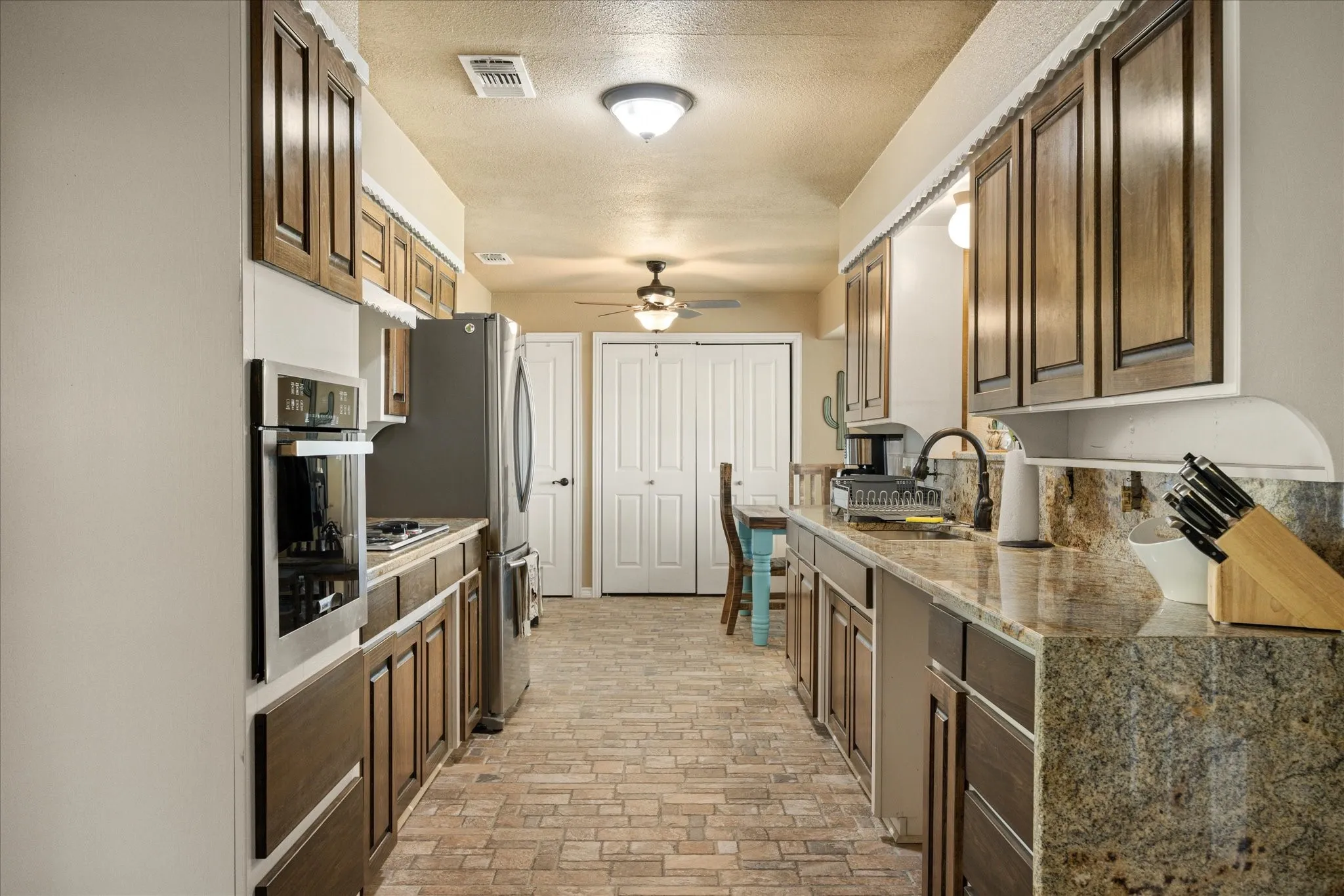 Kitchen featuring stainless steel oven, sink, light stone counters, a textured ceiling, and tasteful backsplash
