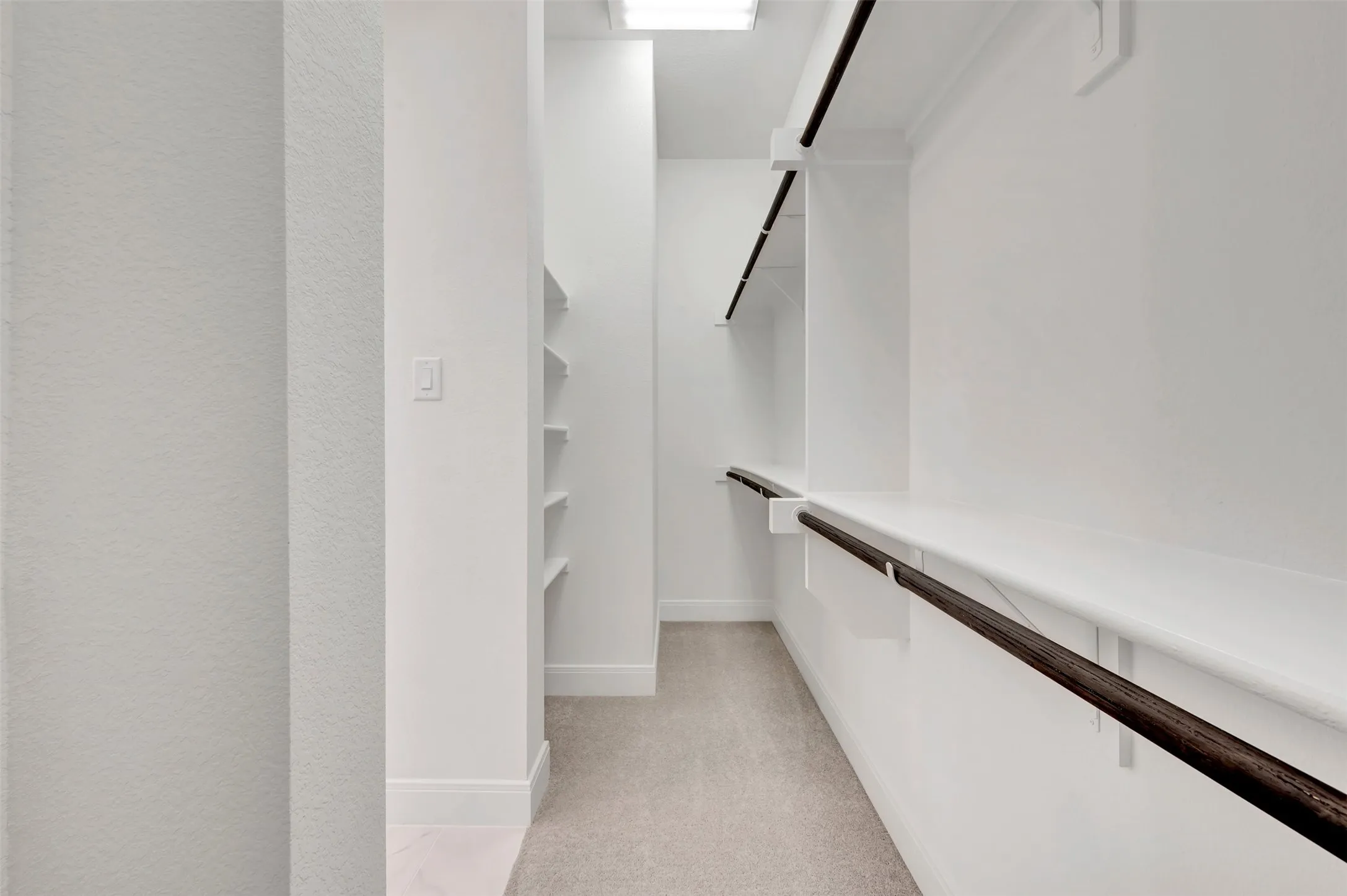 Walk-in closet featuring light-toned carpeting, white shelving, and dark wood-finish hanging rods