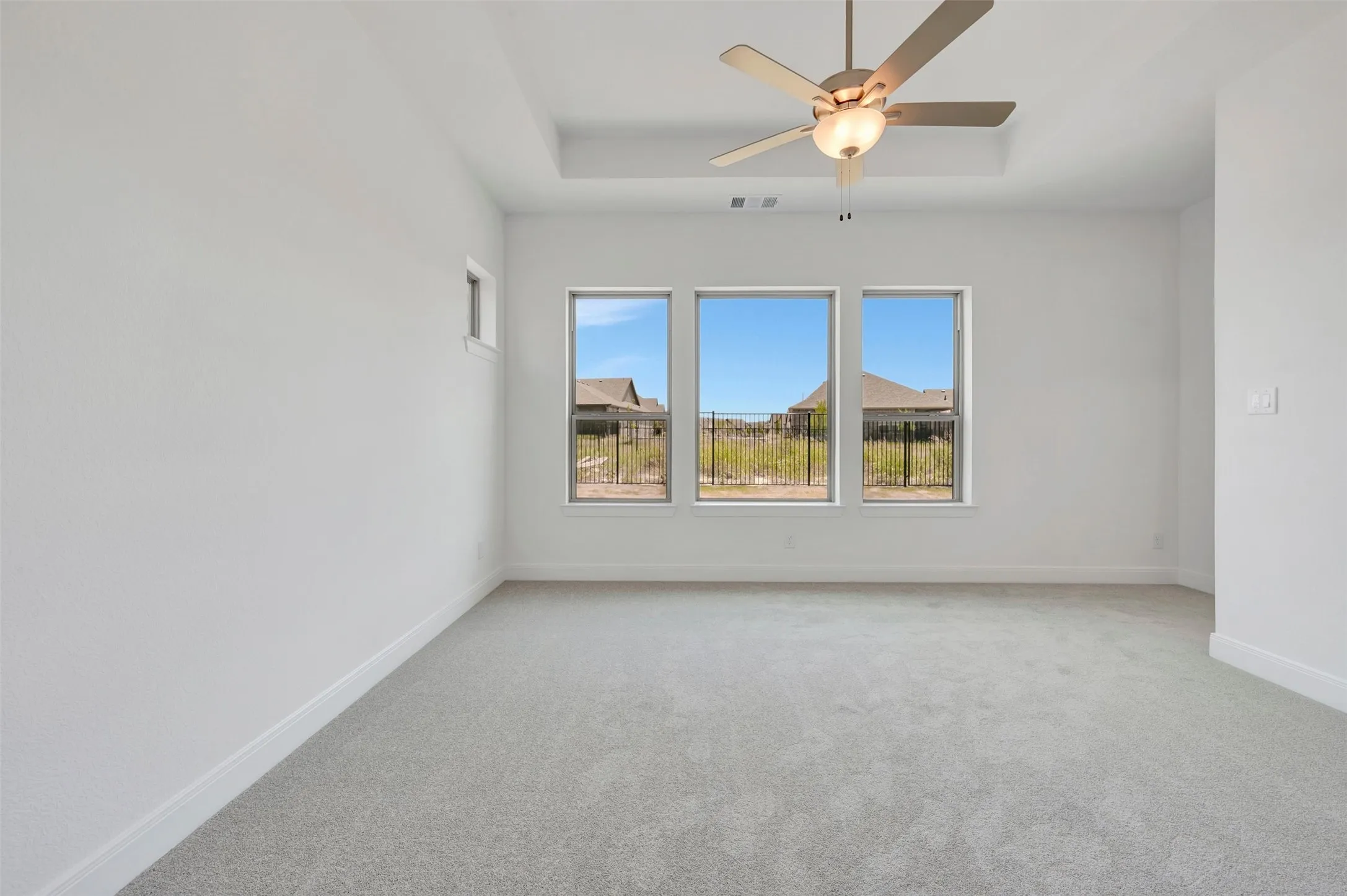 Spacious room featuring light gray carpeting, a tray ceiling, and a ceiling fan with integrated lighting