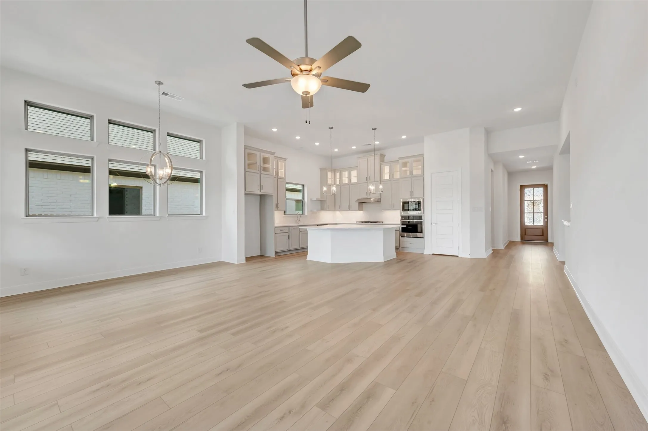 Spacious open-concept living area featuring light wood-finish flooring, a contemporary ceiling fan, and multiple windows