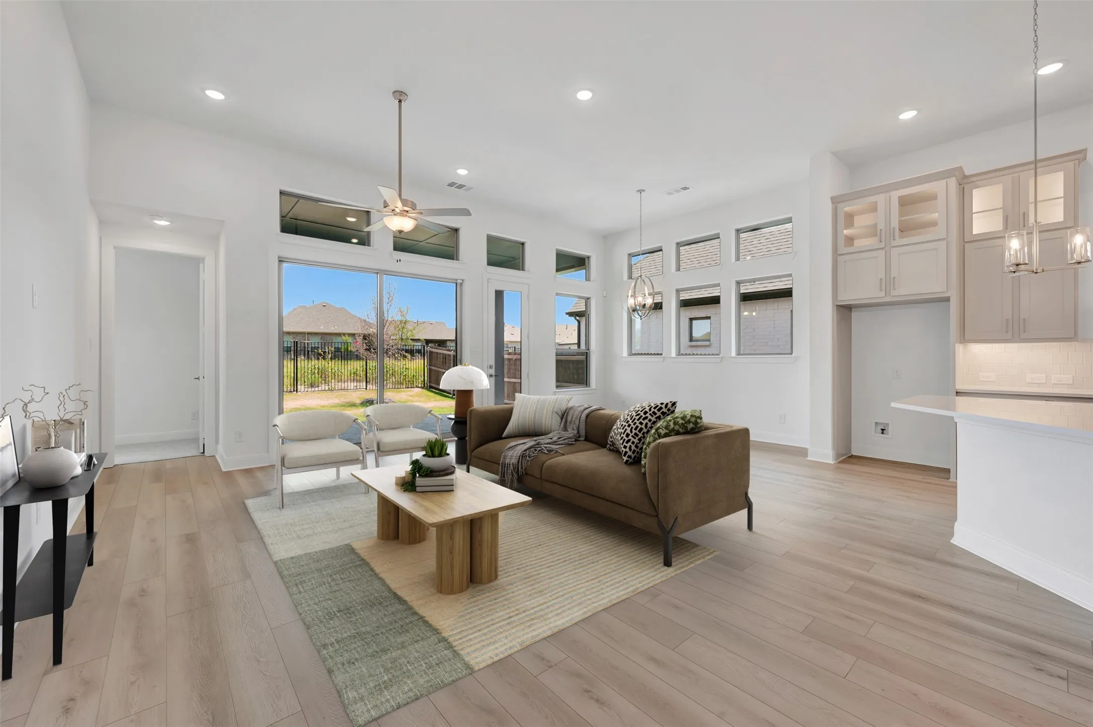 Open-concept living area featuring light wood-finish flooring, vaulted ceilings with recessed lighting, and a ceiling fan