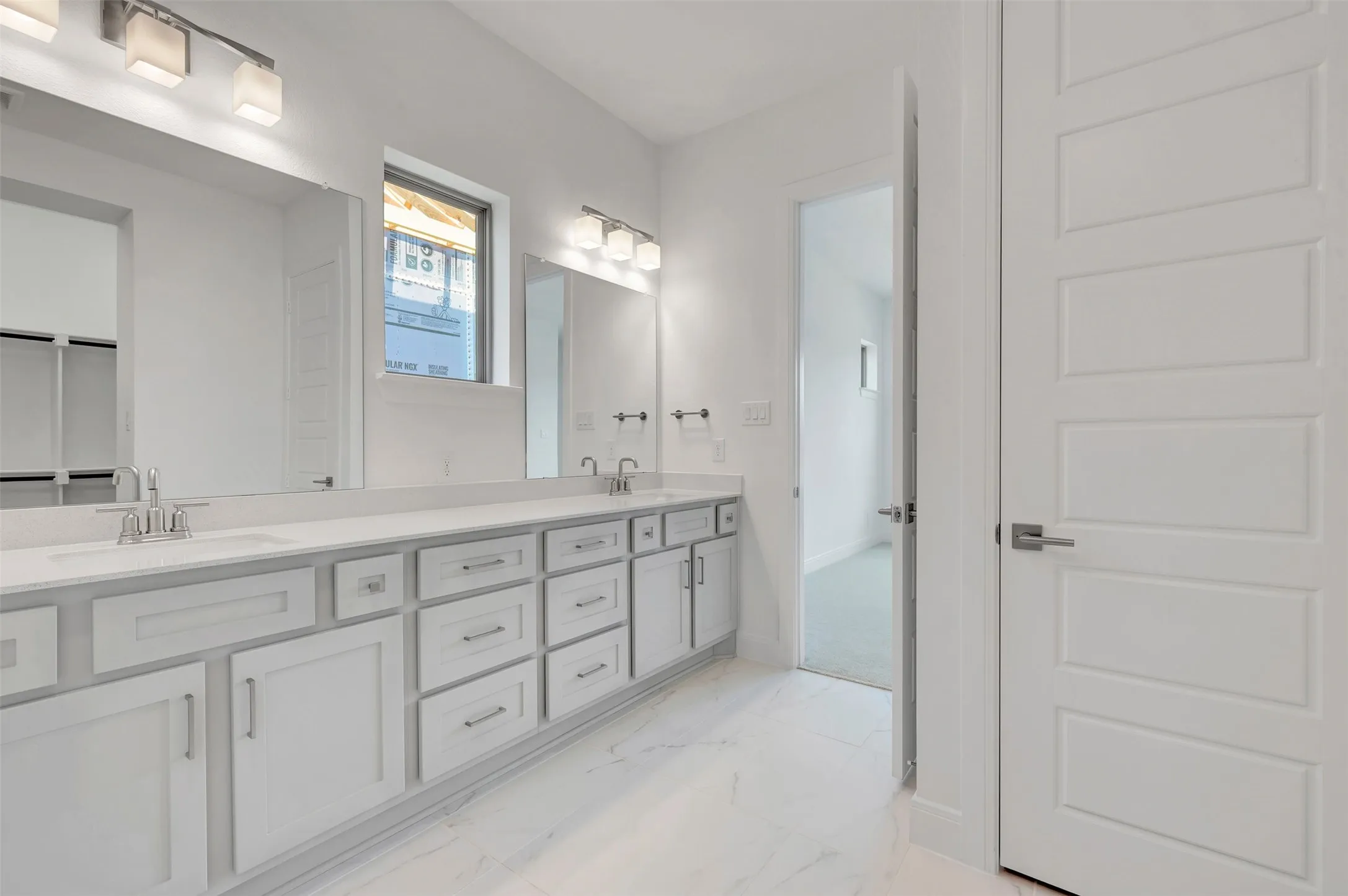 Modern bathroom featuring a double vanity with light gray cabinetry and brushed nickel hardware, set against white walls and a large rectangular window