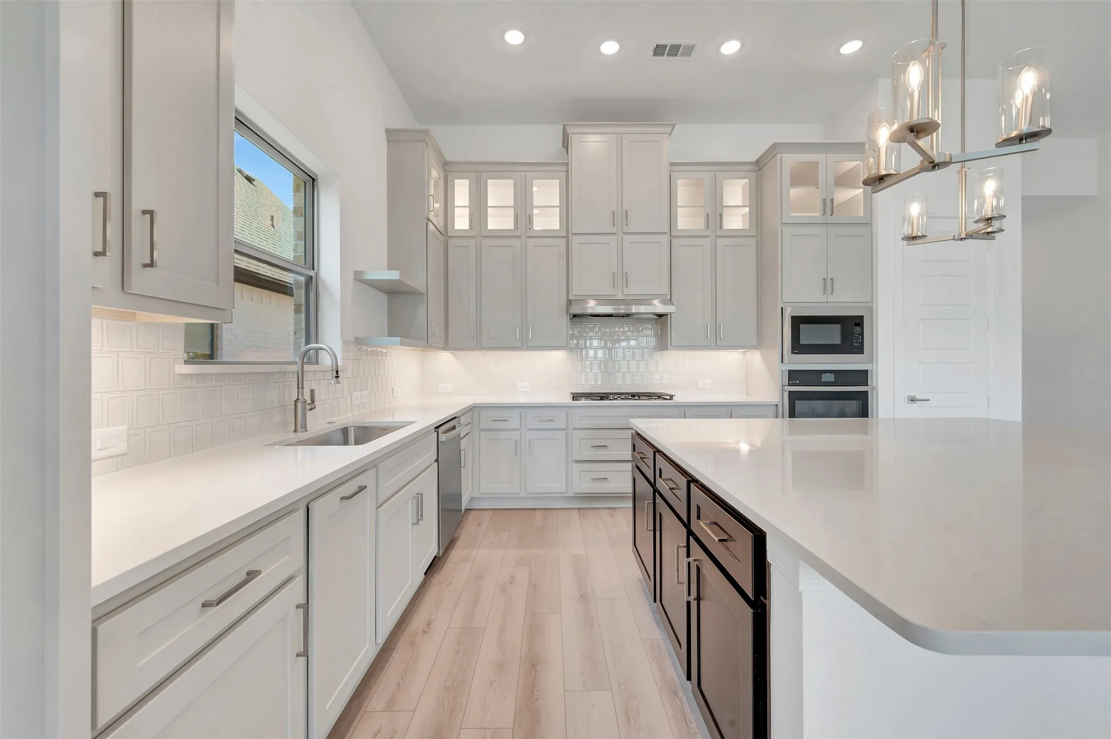 Spacious kitchen featuring an expansive island with a light-toned countertop, wood-finish flooring, recessed lighting, and a modern chandelier