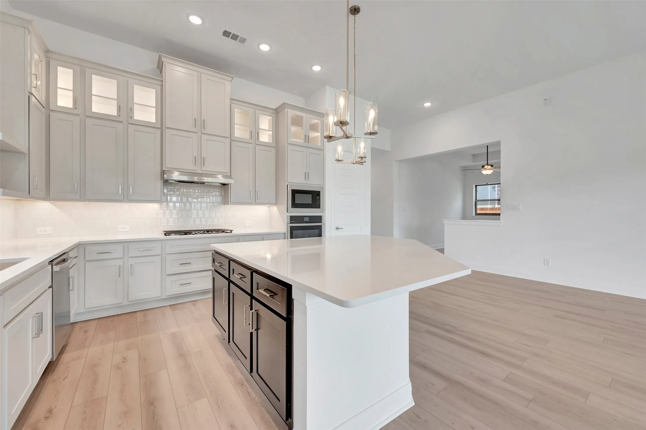 Gourmet kitchen featuring a large island with a solid surface countertop, stainless steel appliances, extensive cabinetry, light wood-finish flooring, and recessed lighting