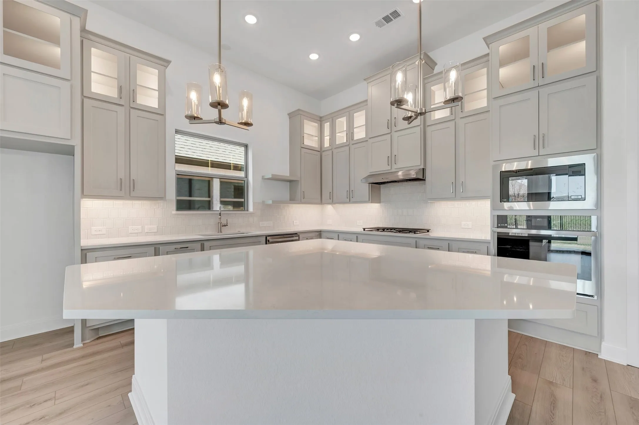 Contemporary kitchen featuring an oversized island with a solid surface countertop, light gray cabinetry, a subway tile backsplash, and stainless steel appliances