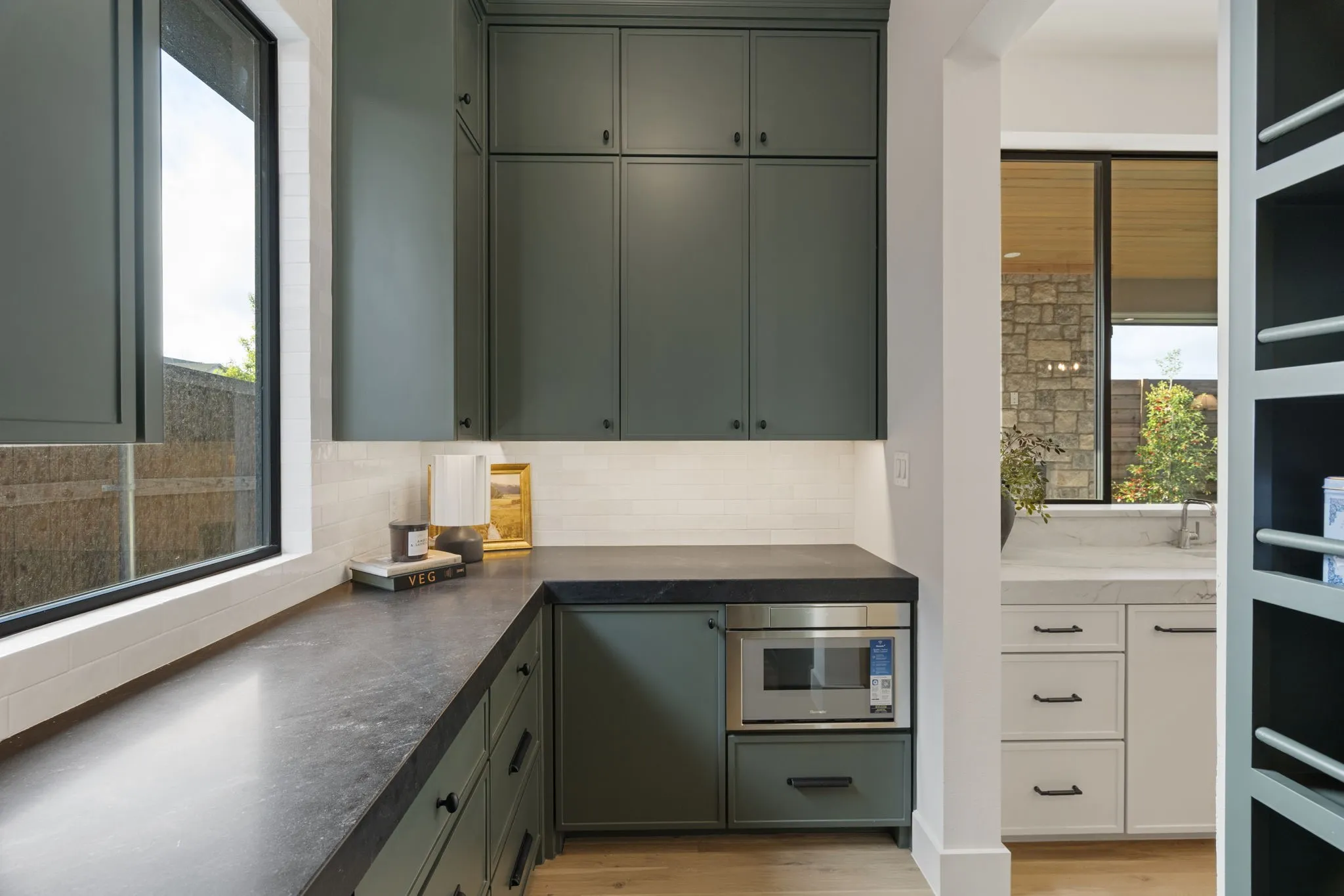 Kitchen with green cabinets, dark countertops, light wood-style floors, and stainless steel microwave