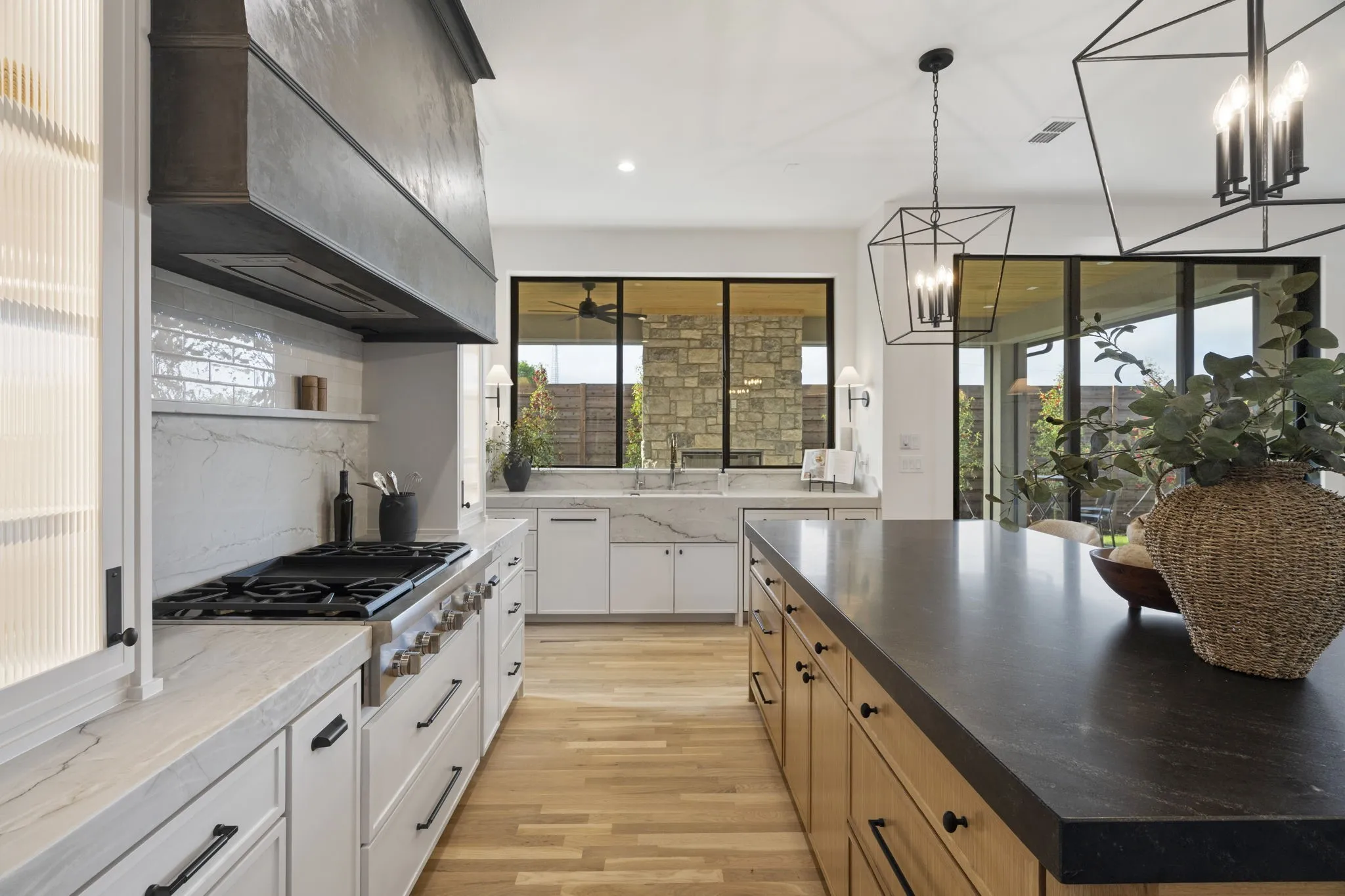 Dual tone kitchen with stainless steel gas cooktop, light wood-style flooring, dark stone countertops, backsplash, and pendant lighting