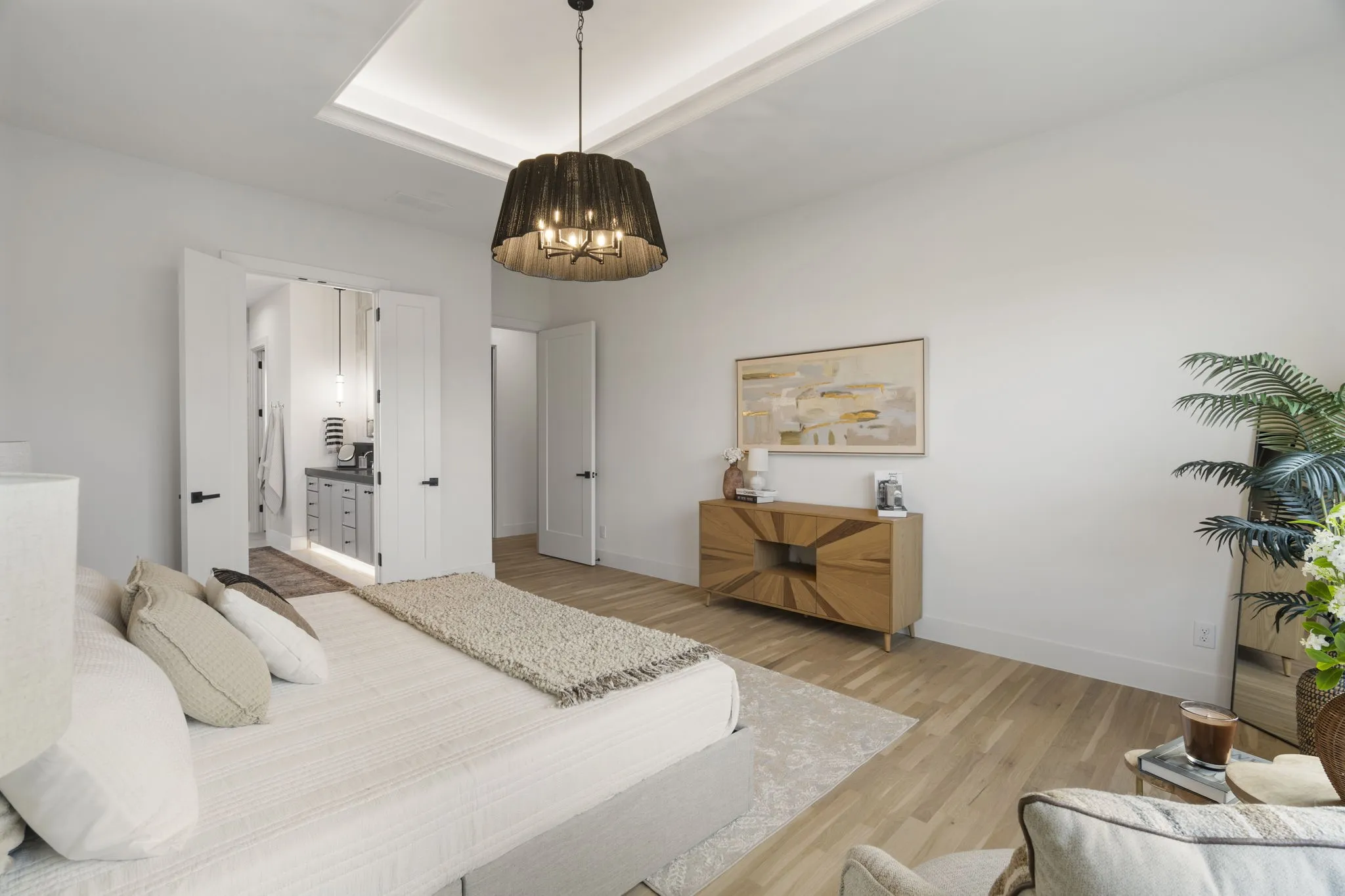 Bedroom with ensuite bathroom, a raised ceiling, and light wood-type flooring