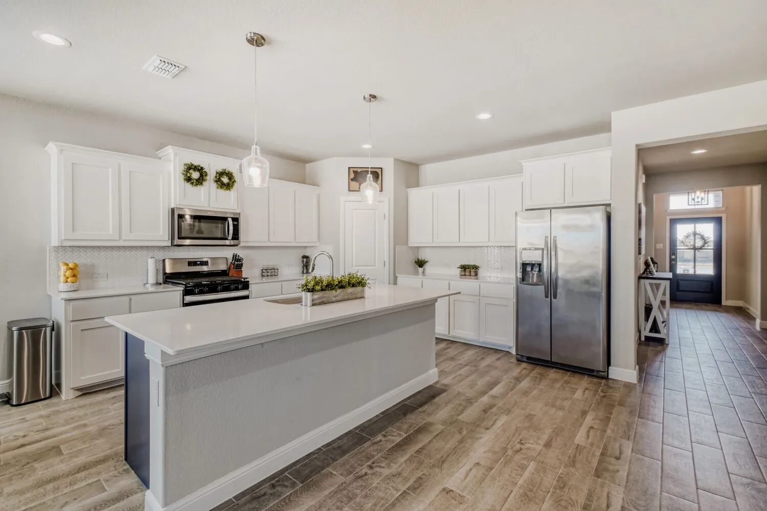Kitchen featuring stainless steel appliances, white cabinets, light wood finished floors, decorative light fixtures, and a center island with sink