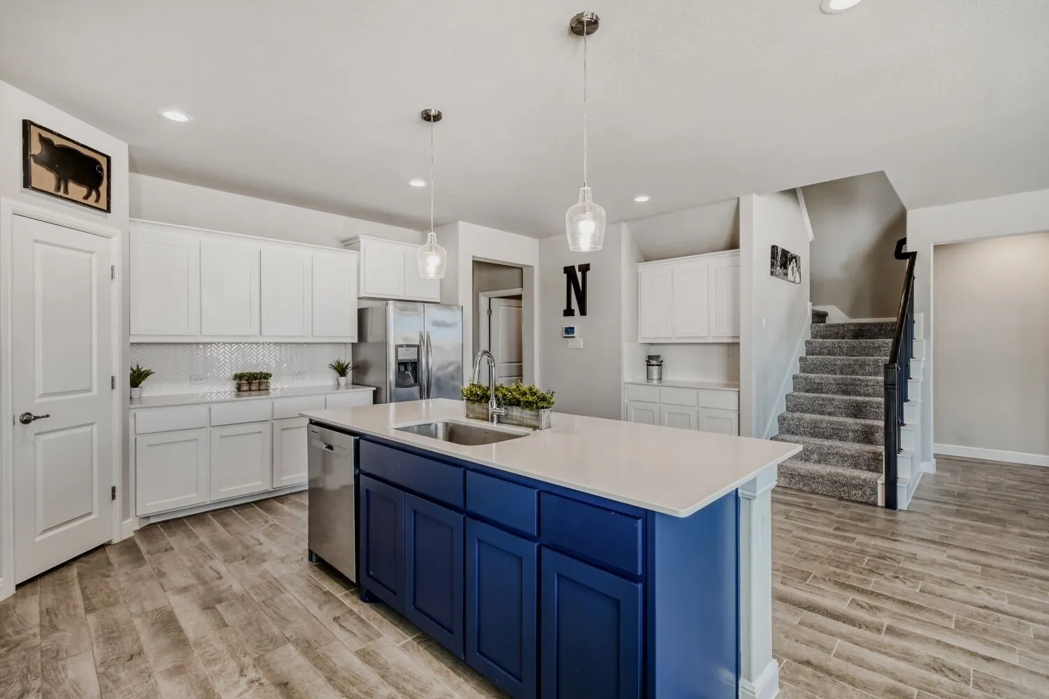 Kitchen featuring two tone cabinetry, pendant lighting, stainless steel appliances, light wood-type flooring, and a kitchen island with sink