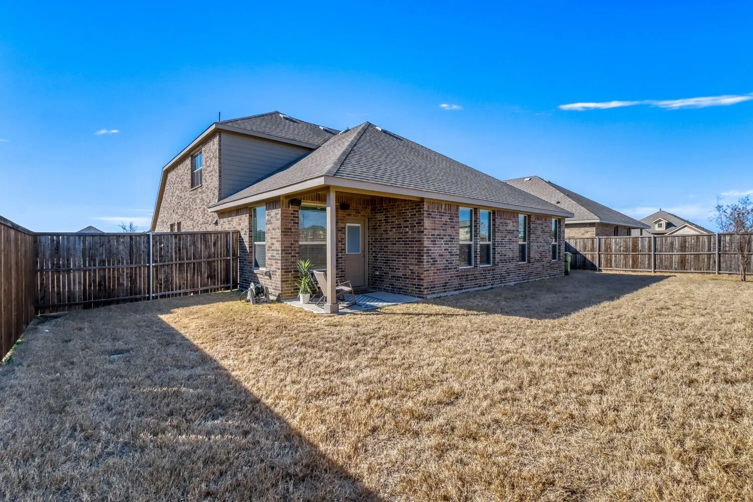 Back of property with a patio area, a shingled roof, brick siding, and a fenced backyard
