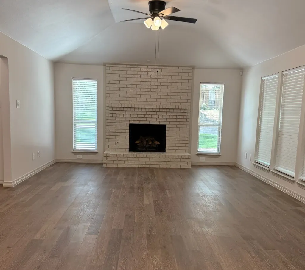 Living room with lofted ceiling, ceiling fan, wood finished floors, and a fireplace